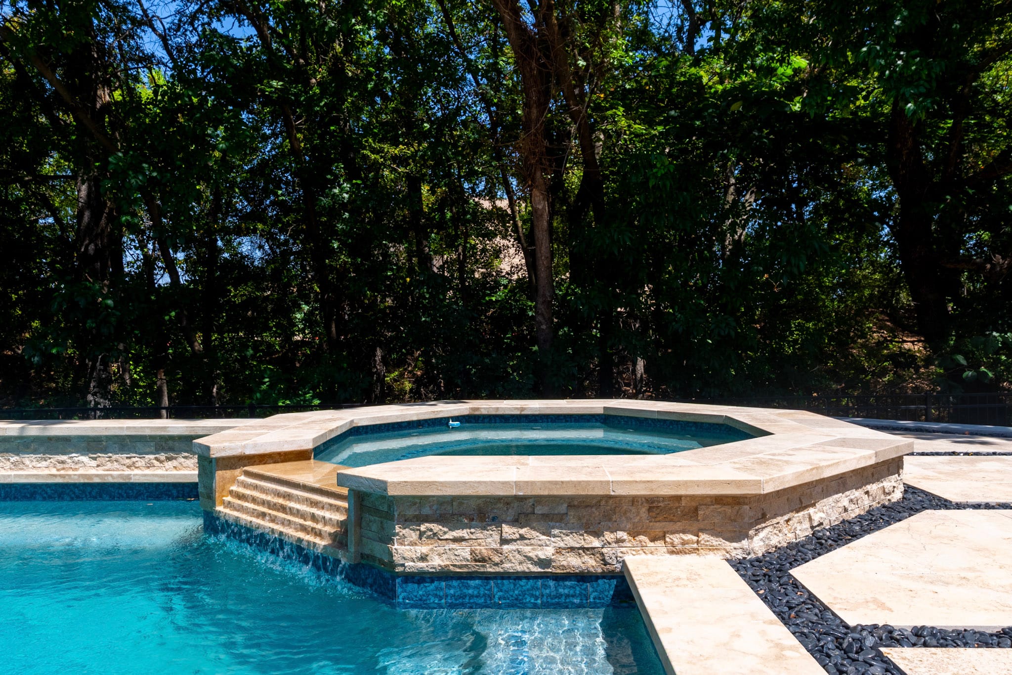 Raised multi-sided spa with stone veneer and light coping beside a McKinney swimming pool.