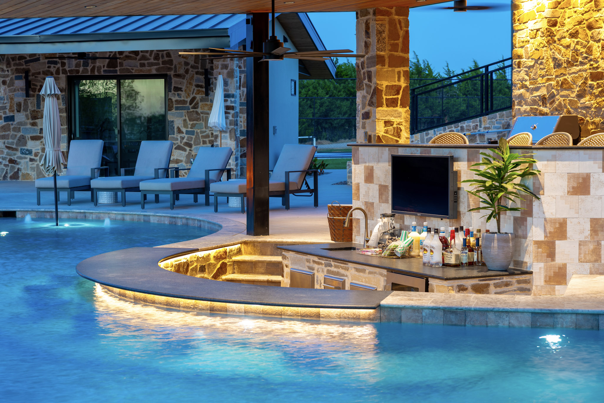 Sunken swim-up pool bar with television, sink and curved counter.