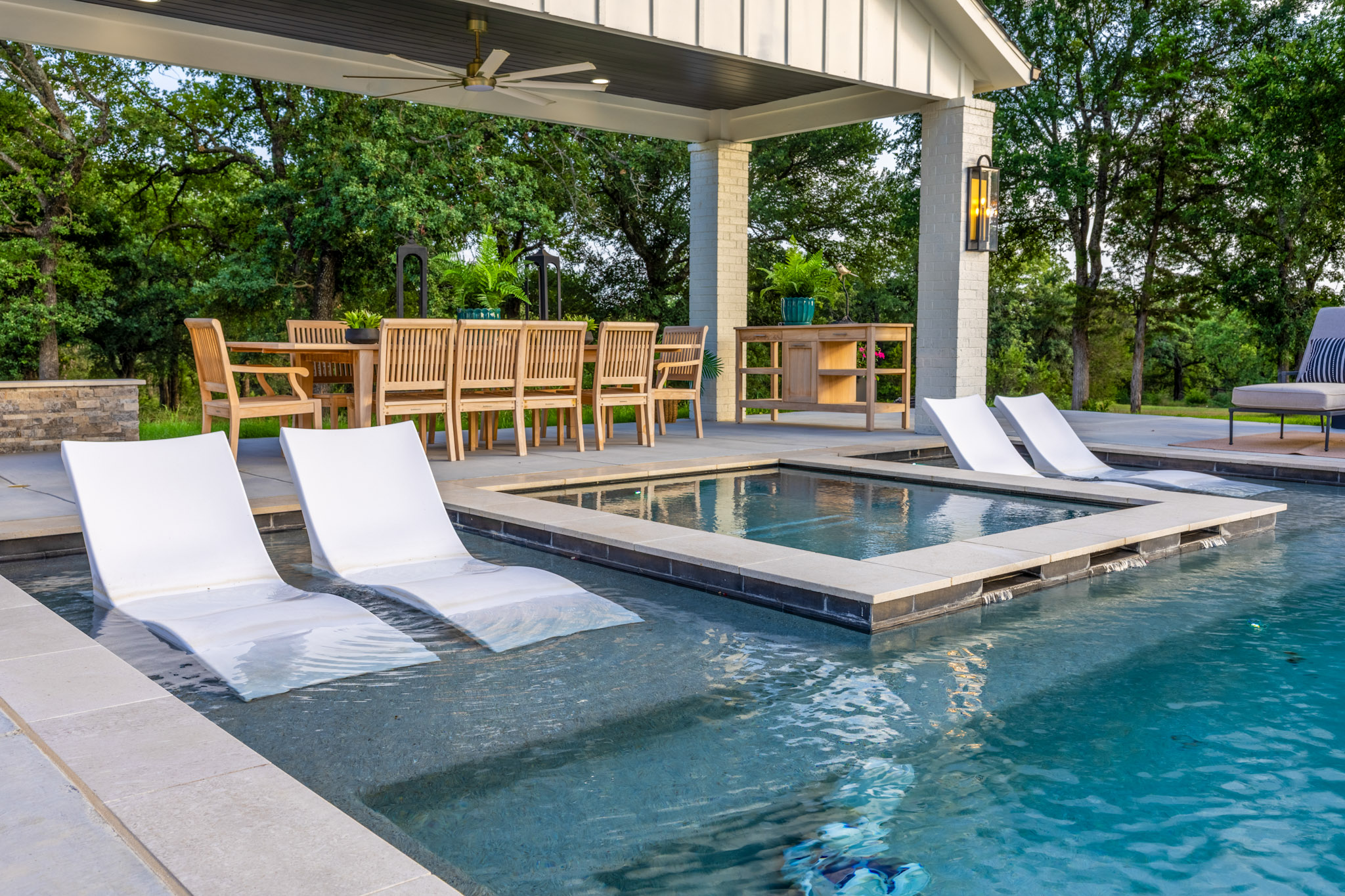Rectangular pool water feature surrounded by submerged loungers beneath a dining pavilion.