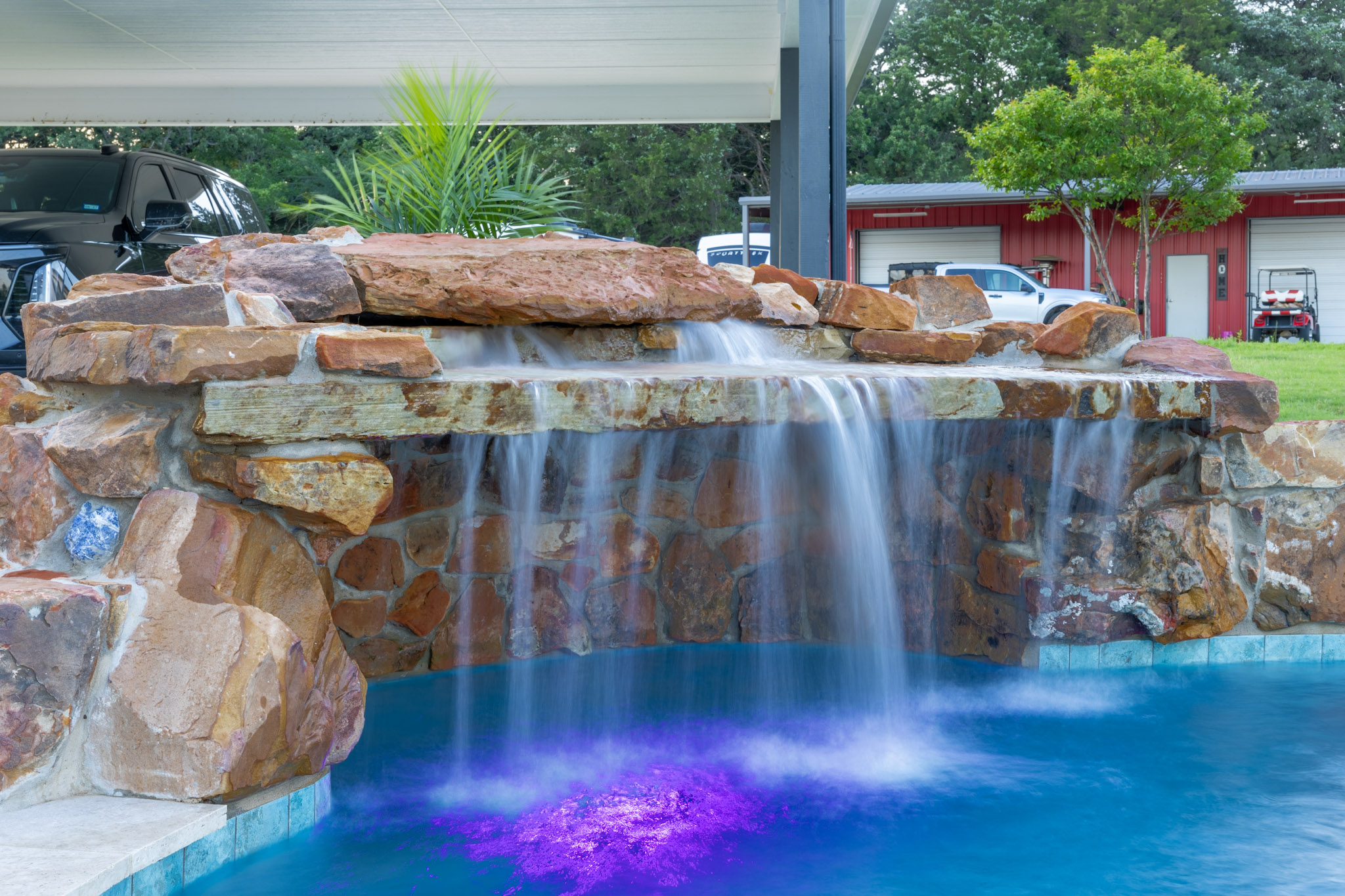Wide natural stone waterfall cascading into a blue pool with purple underwater lighting.