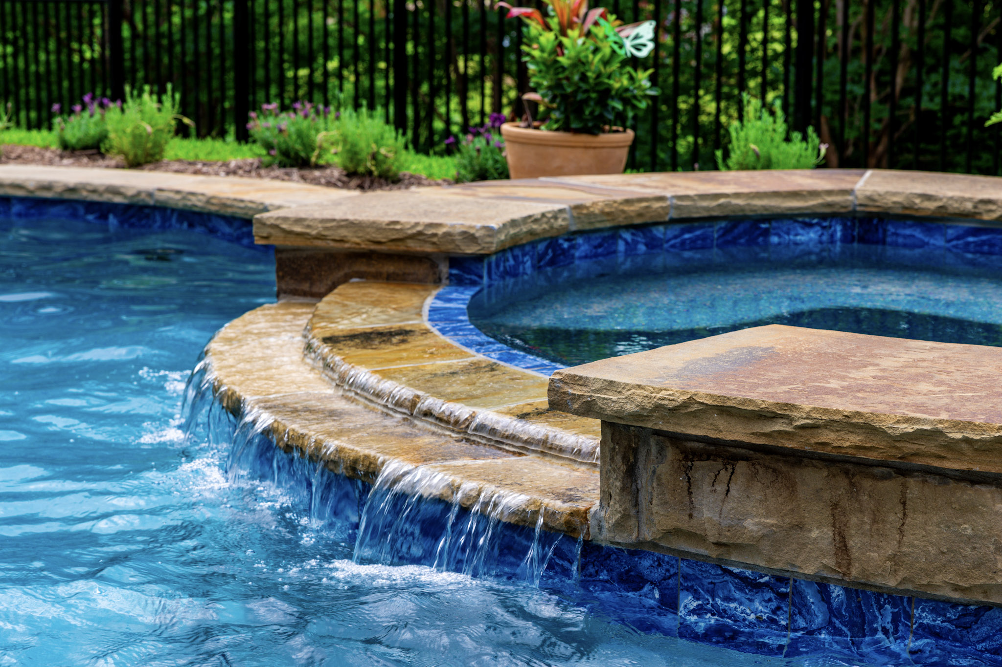 Raised circular spa with stone coping and curved spillway flowing into the pool.