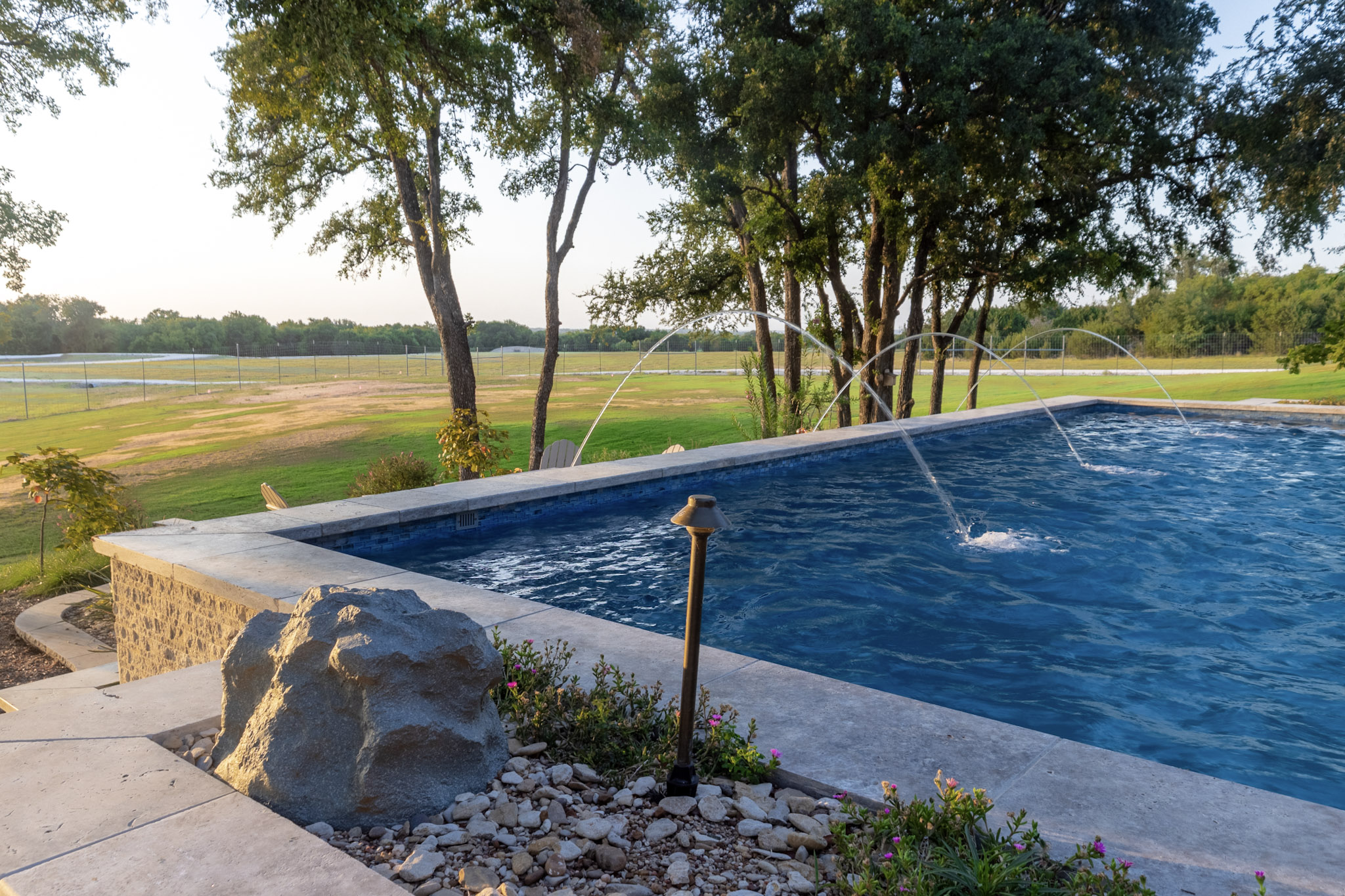 Laminar jets crossing a raised pool with stone coping and ranch views.