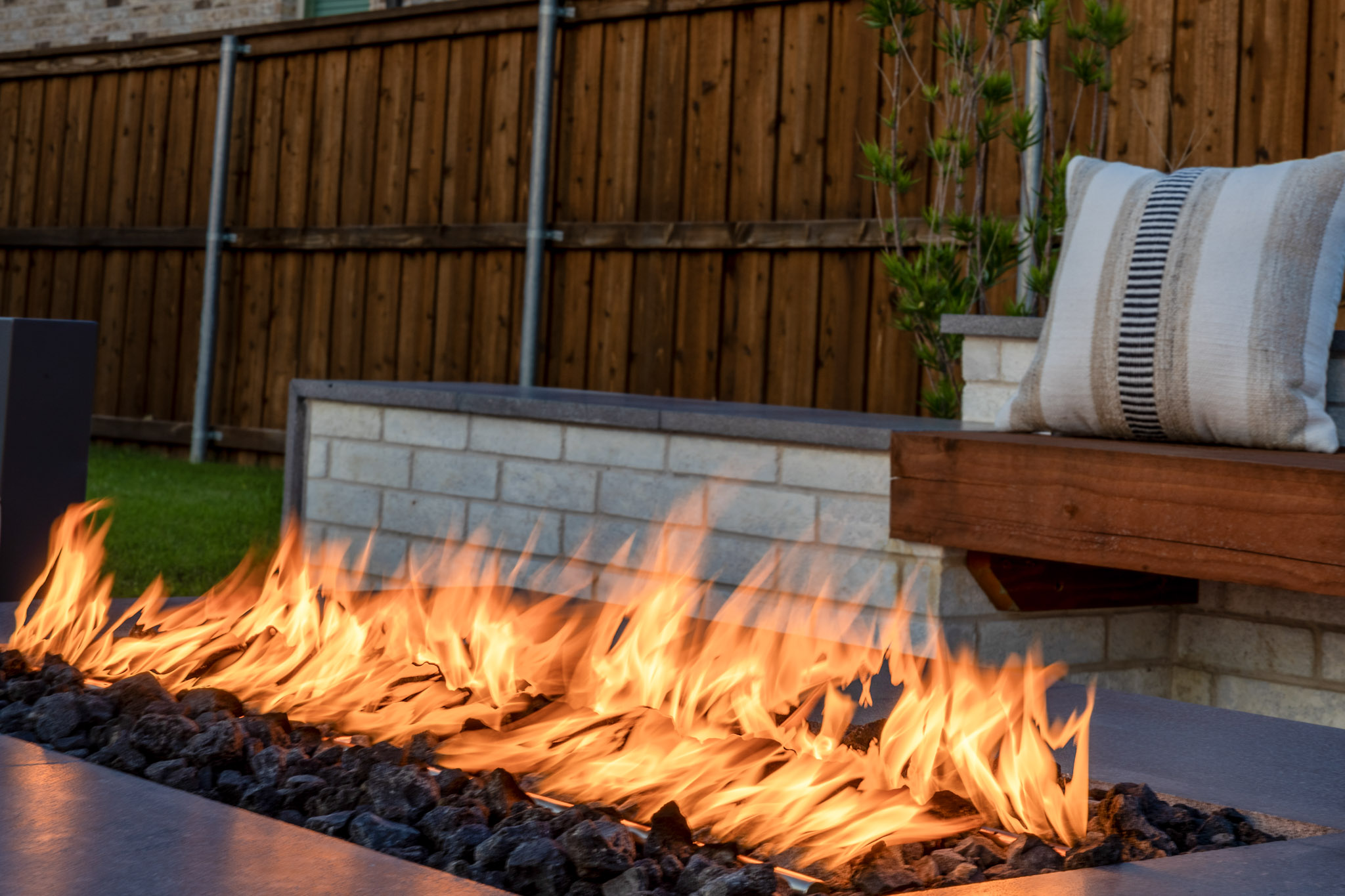 Close-up of modern gas fire feature with lava rock beside custom outdoor seating.