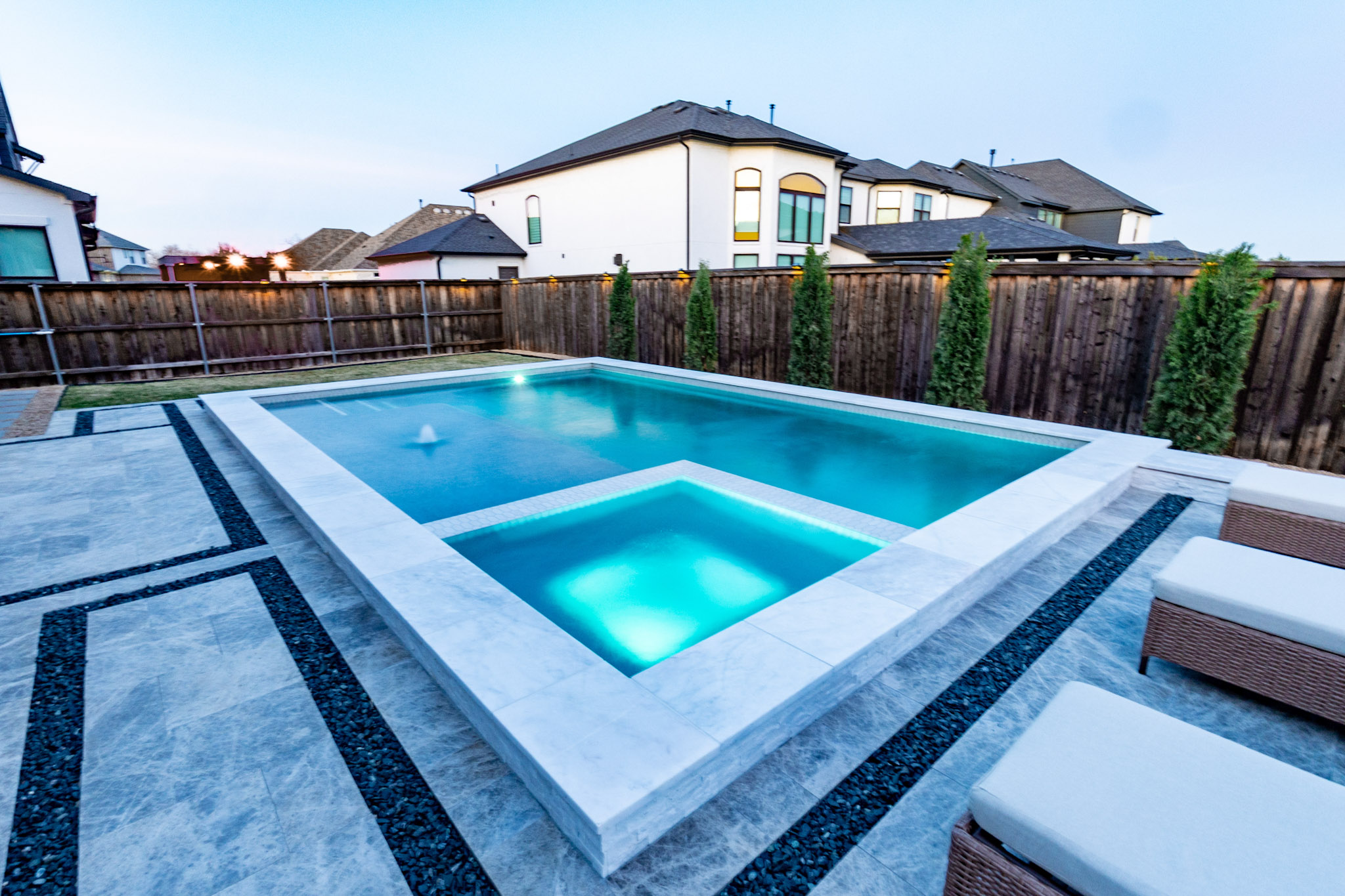 Blue-lit rectangular pool and square spa at twilight beside a modern home.