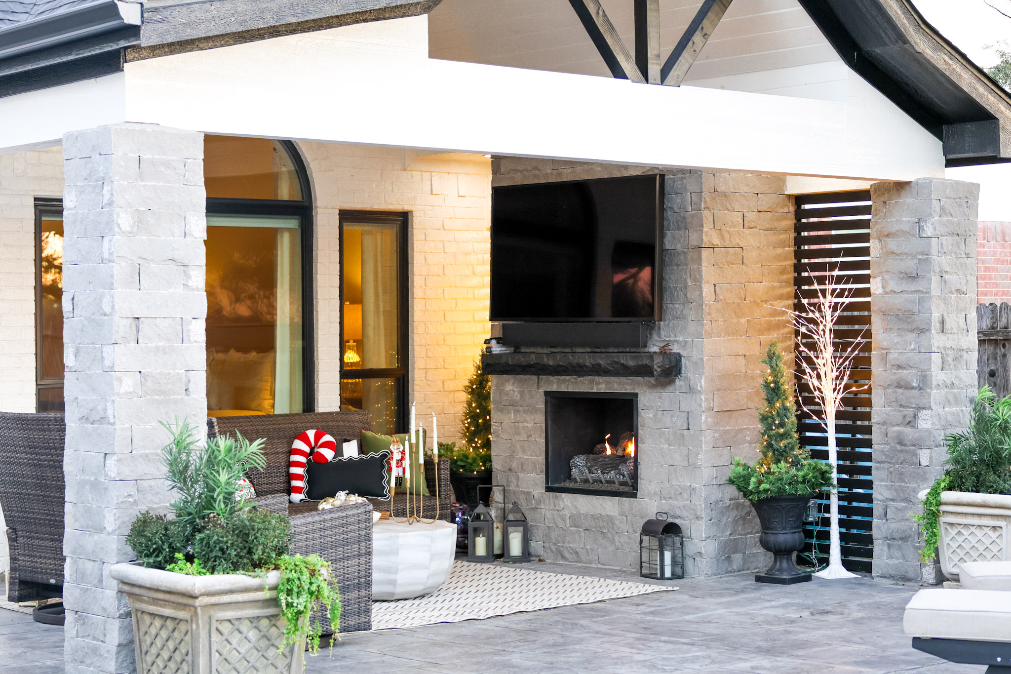 Covered outdoor living area with stone fireplace, television, seating and pool in the foreground.