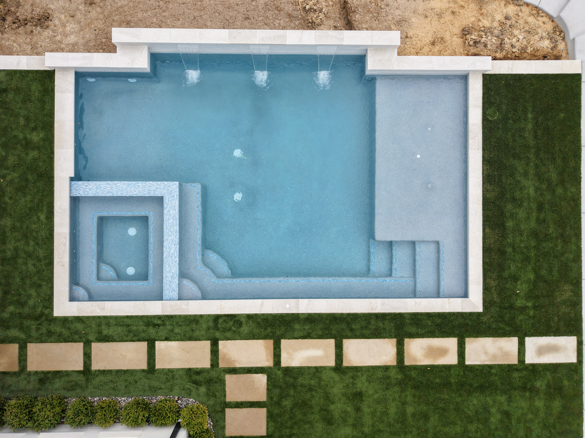 Top-down aerial of geometric pool with spa, tanning ledge, steps and three sheer descents.
