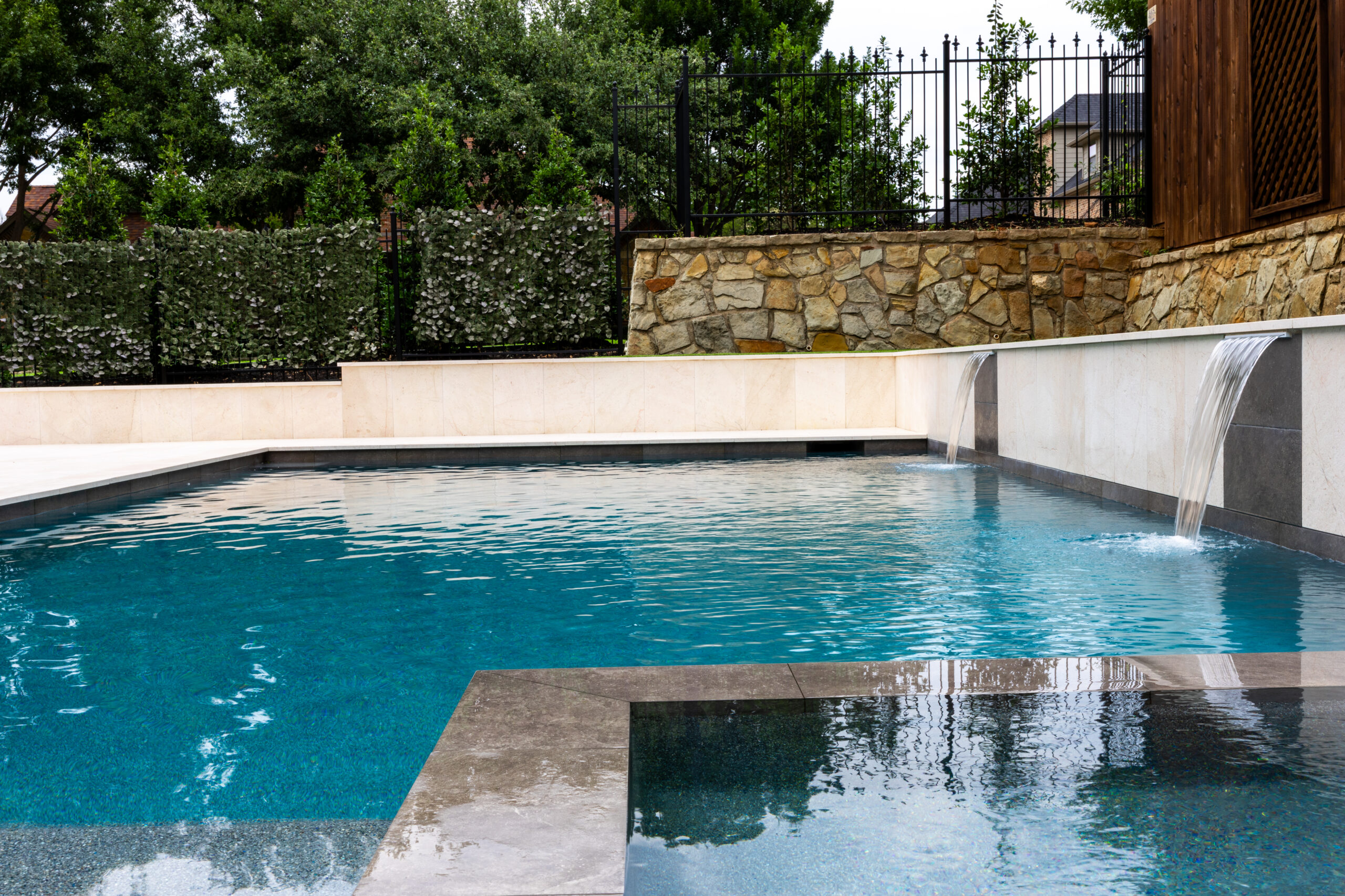 Integrated spa overlooking modern swimming pool with dual sheer descent water features in Colleyville, Texas.