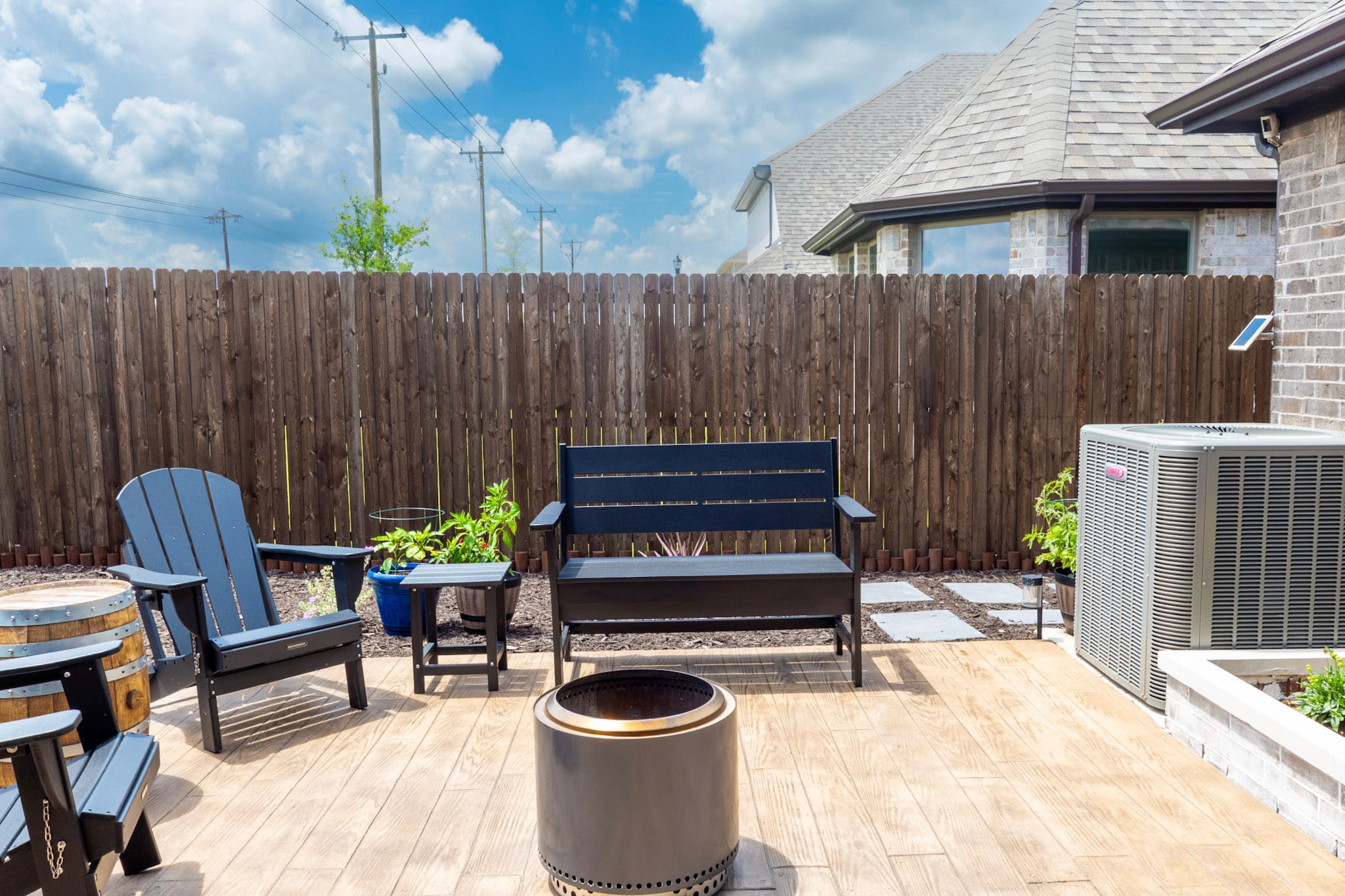 Open backyard patio with black outdoor seating, circular fire pit and surrounding landscaping.