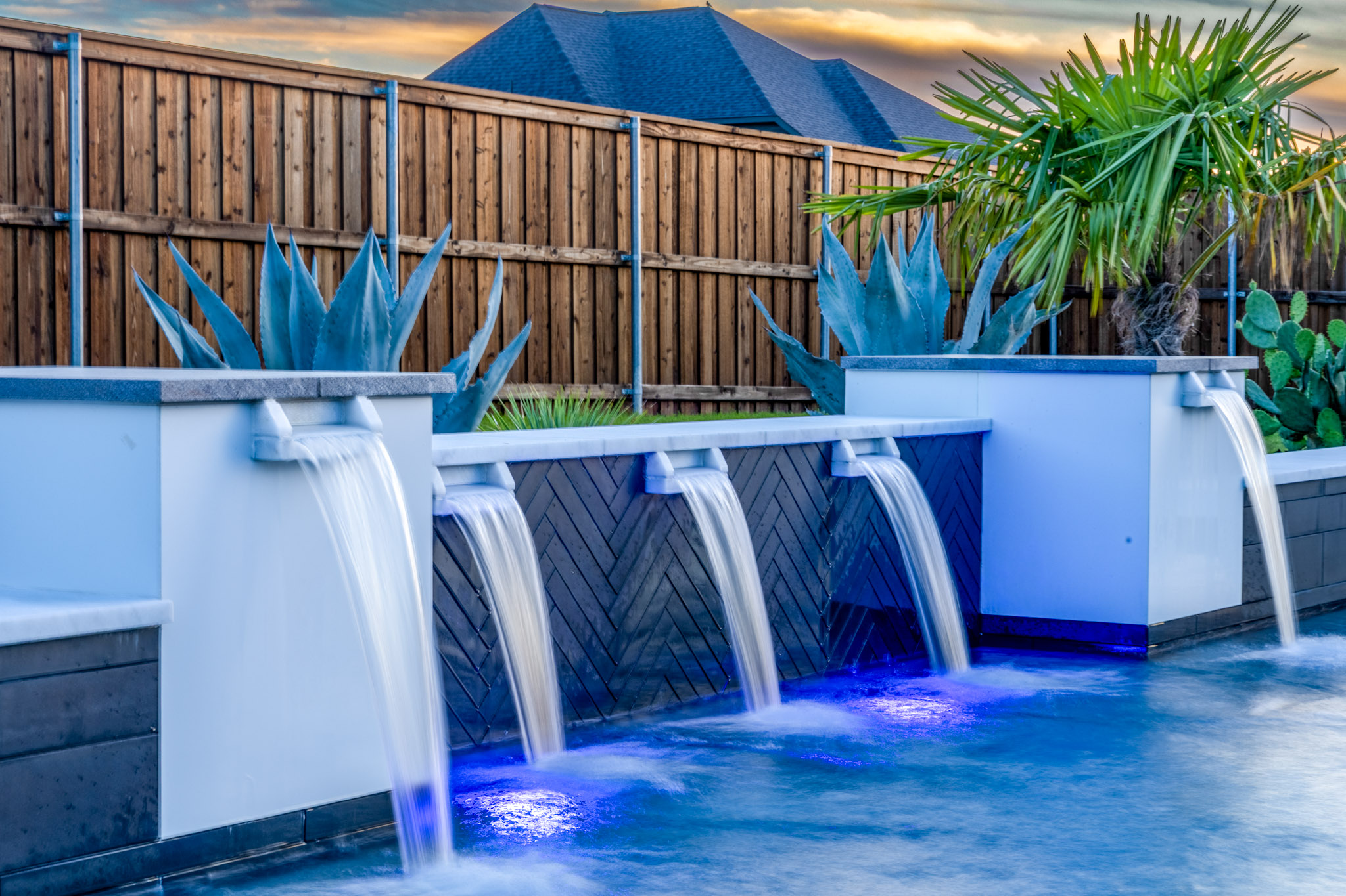 Modern pool water features with herringbone tile, agave plants and palm trees.