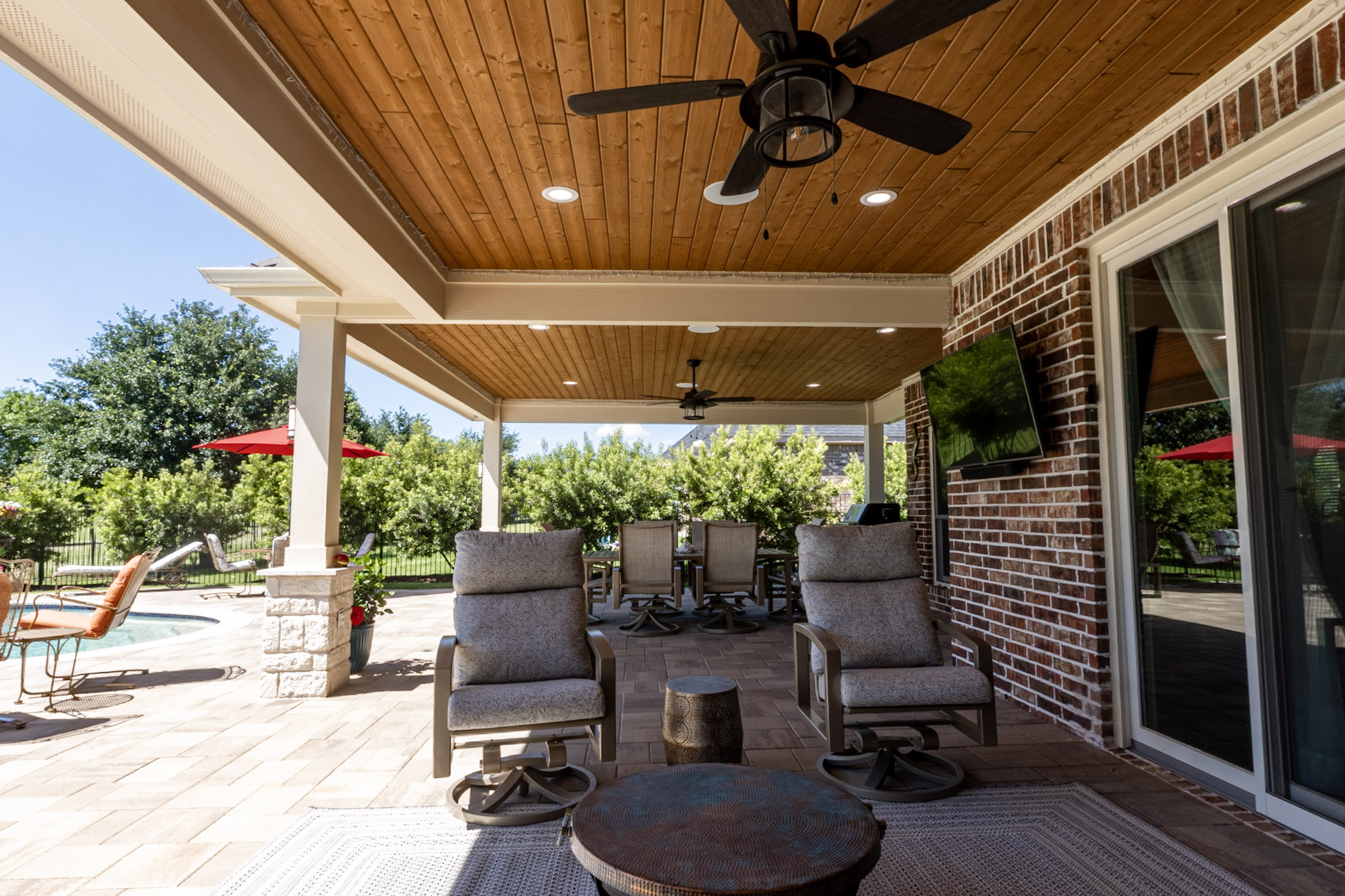 Large covered patio with wood-plank ceiling, ceiling fans, recessed lights and outdoor dining furniture.
