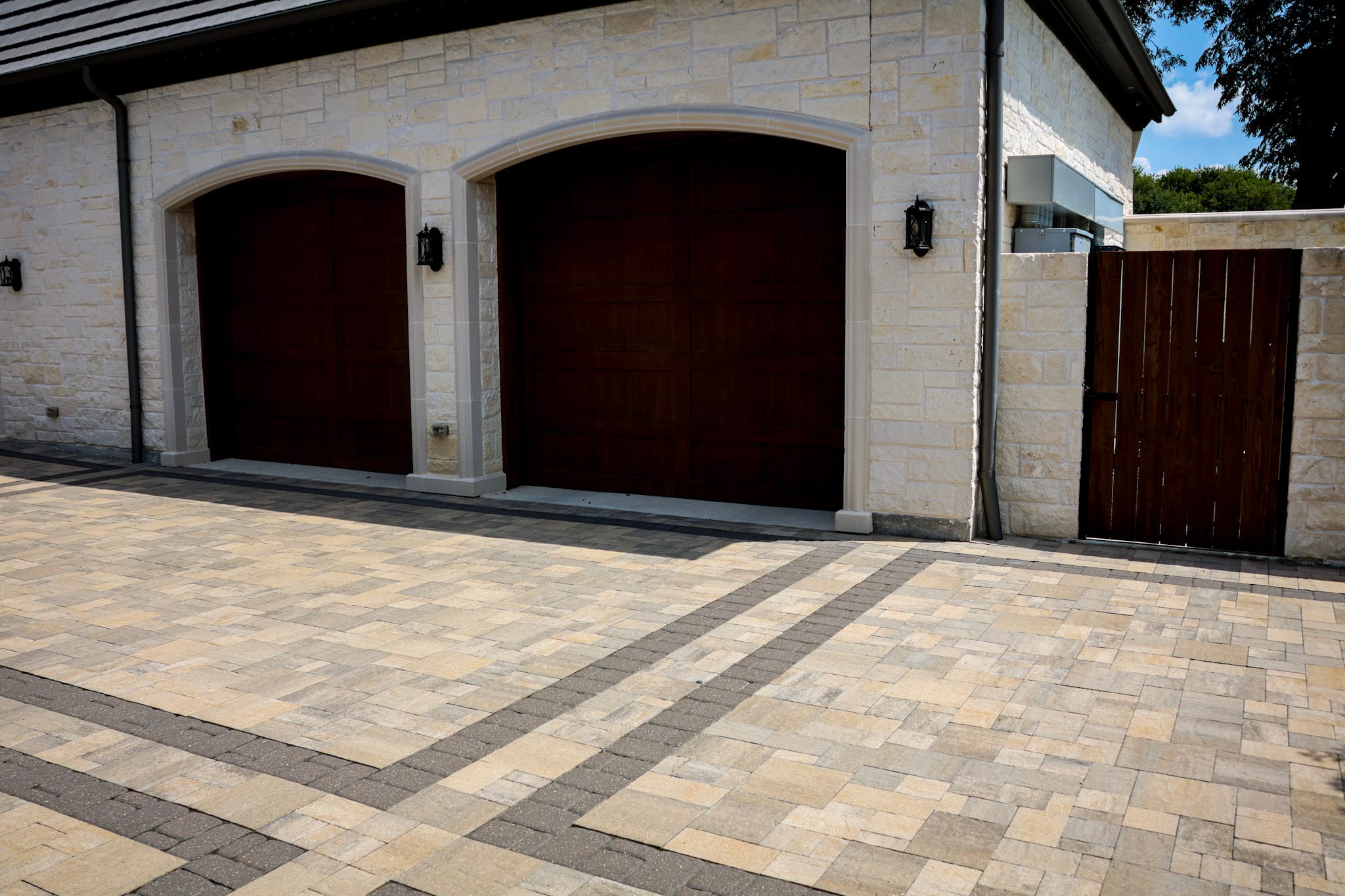 Belgard paver driveway with dark border accents in front of two arched wood garage doors.