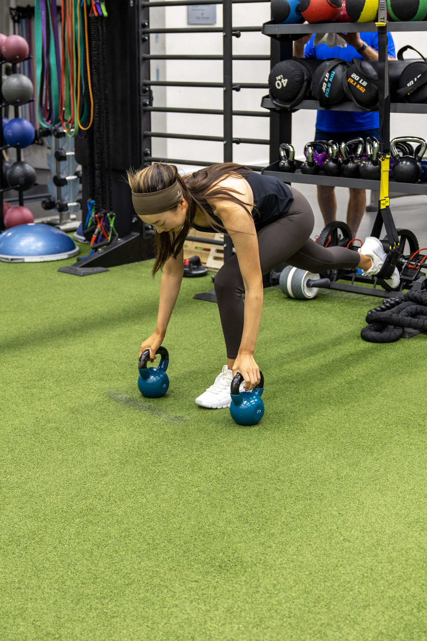 Athlete reaching toward two kettlebells while balancing on one leg with suspension support.