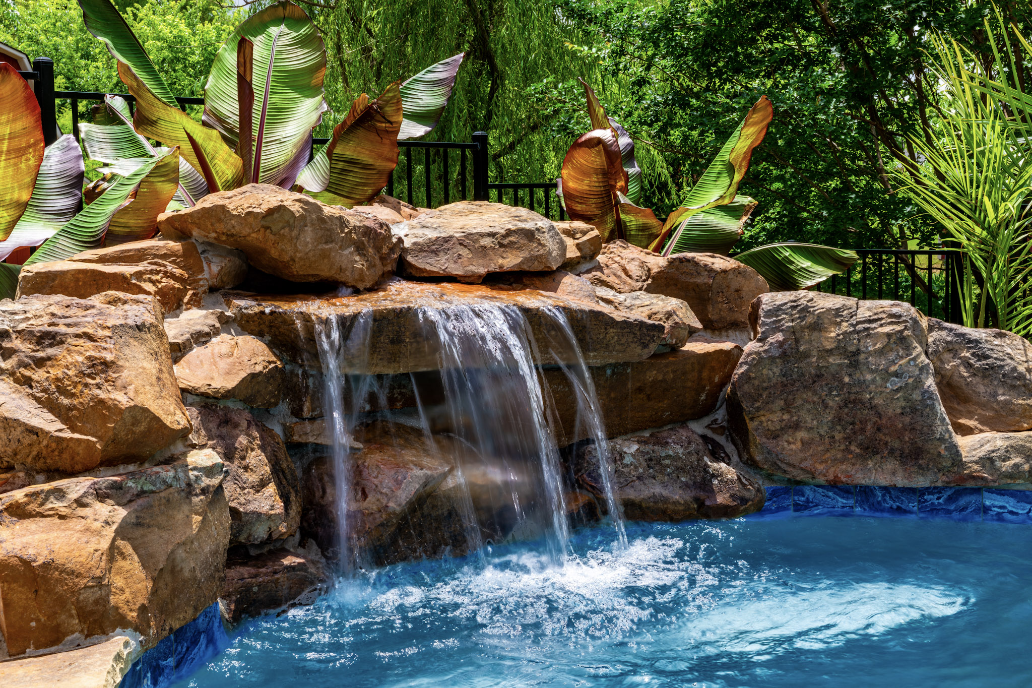 Close view of water cascading over natural rocks into a swimming pool.