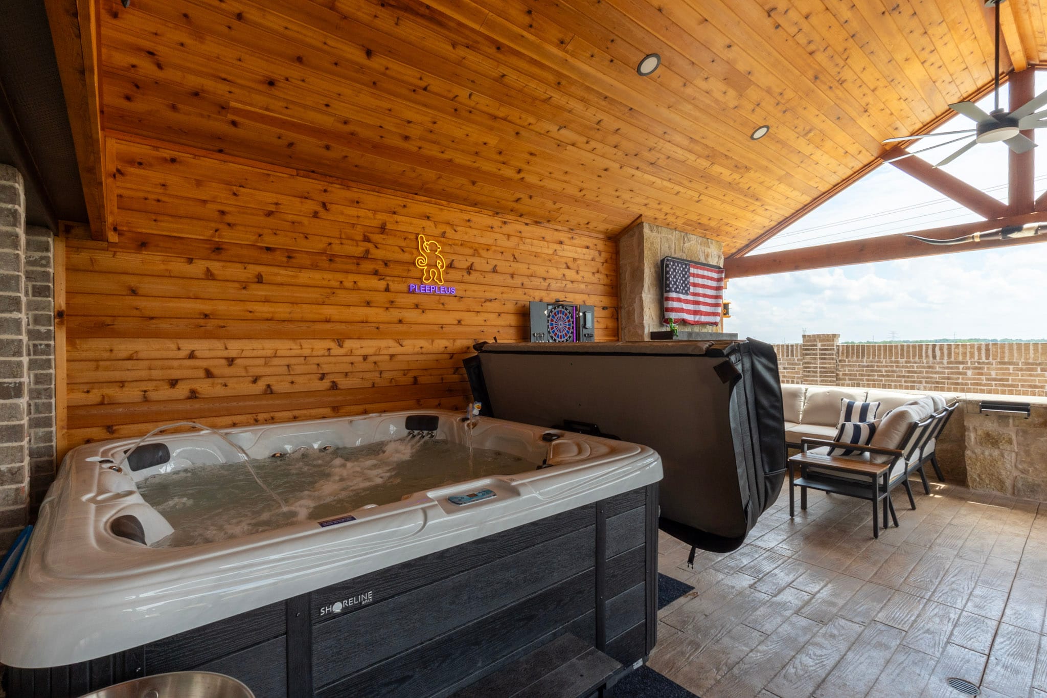 Hot tub beneath a wood-clad covered patio with a stone fireplace and outdoor seating.
