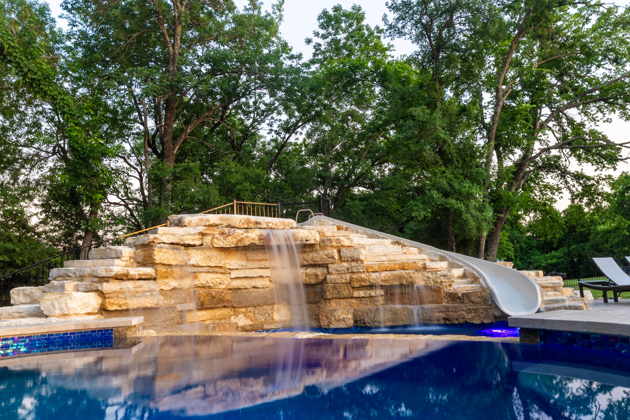 Natural stone pool waterfall and integrated slide at custom Weston, Texas landscape project