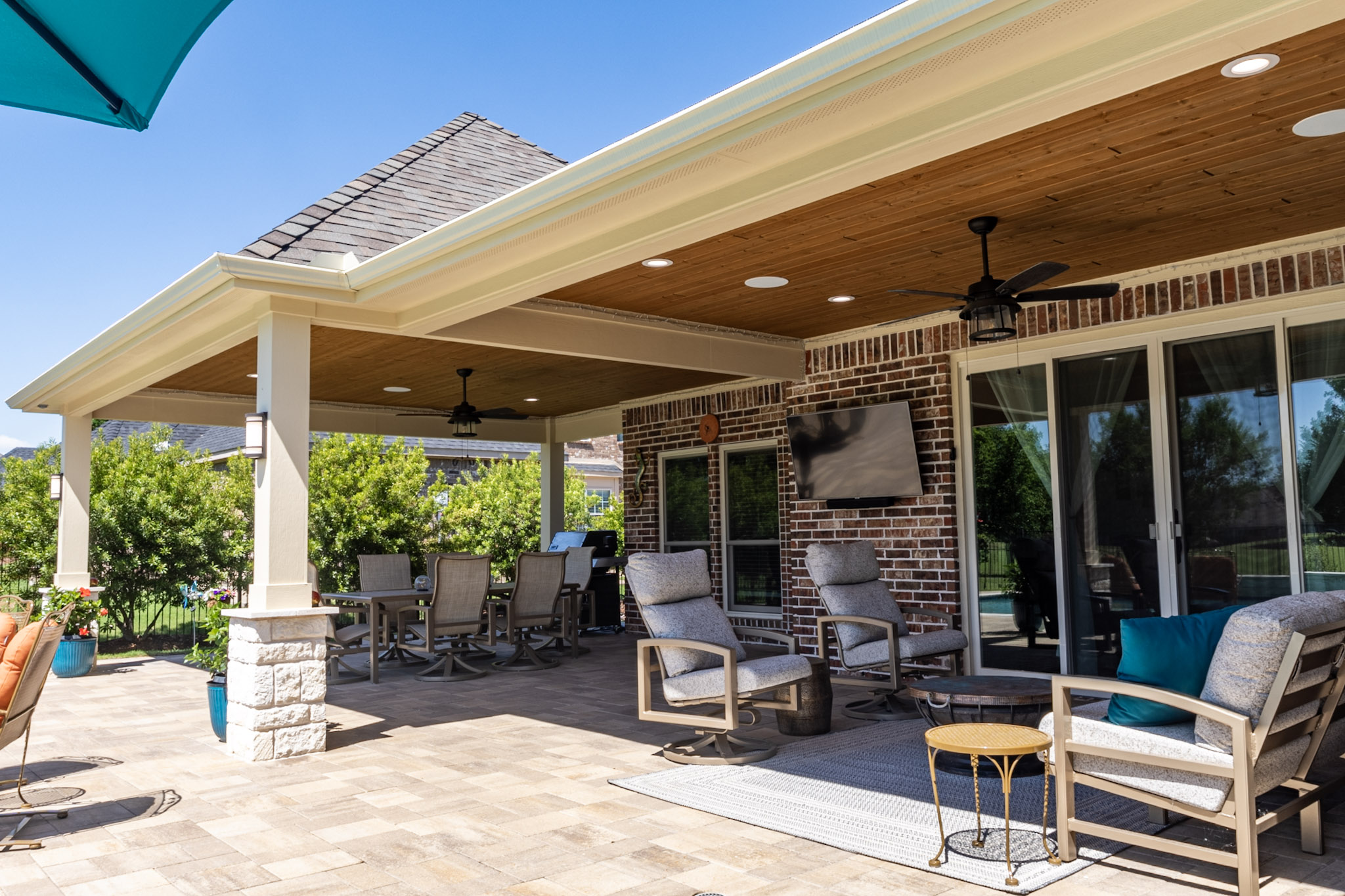 Expanded covered patio with wood ceilings, dining area, lounge seating and stone-base columns.