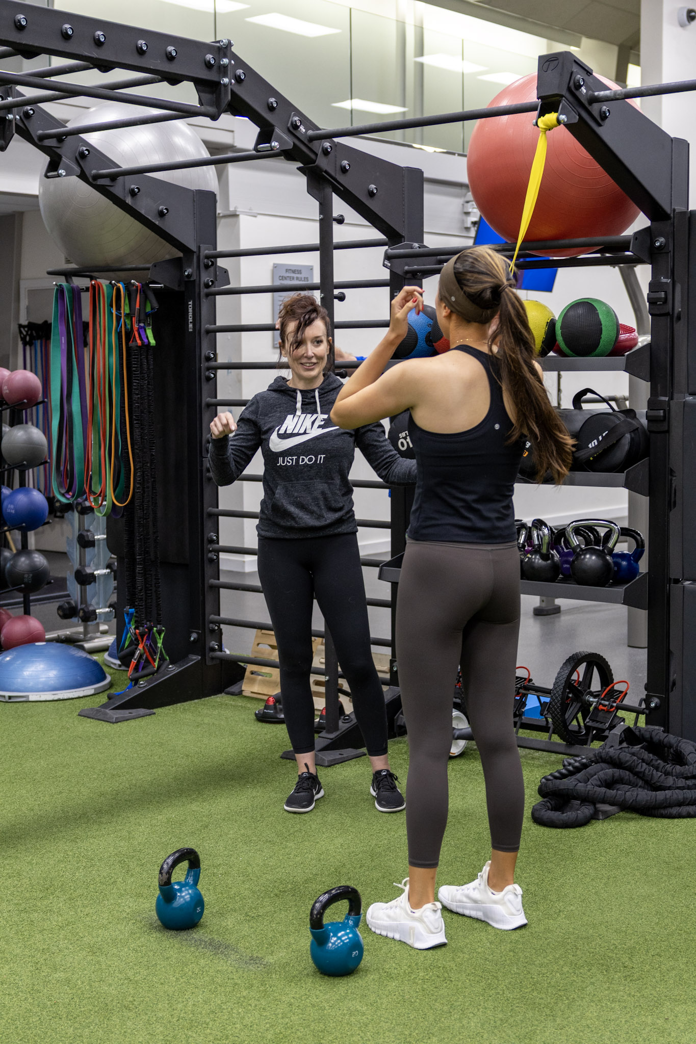 Athlete standing beside her strength coach with kettlebells and training equipment nearby.