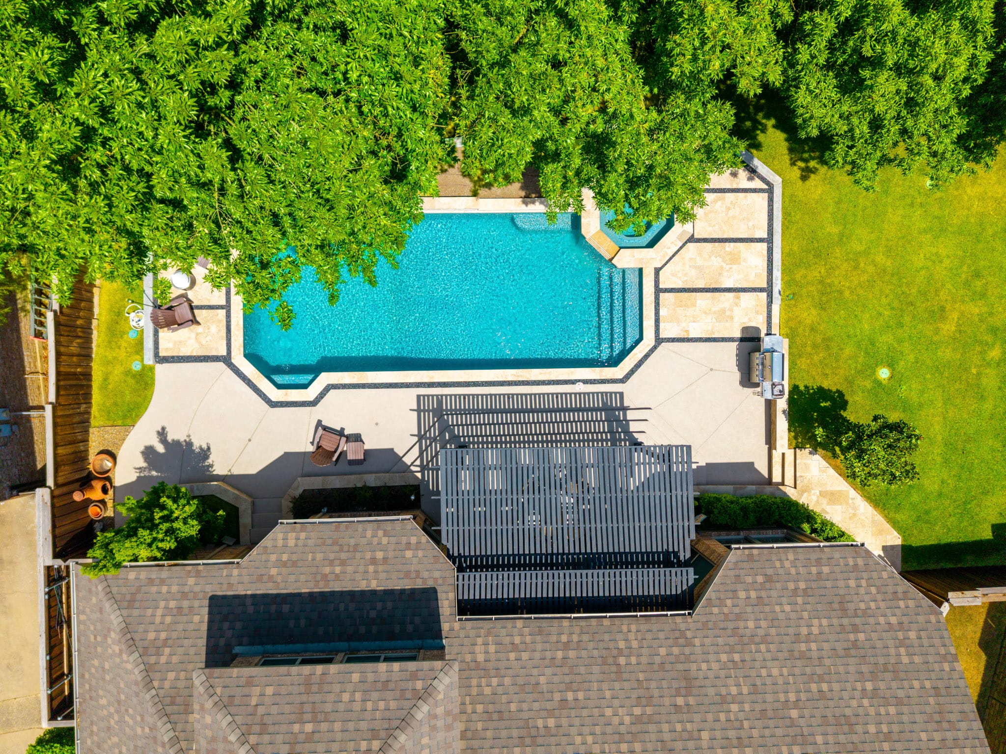 Straight-down drone view of a geometric pool, raised spa, pergola and surrounding backyard.