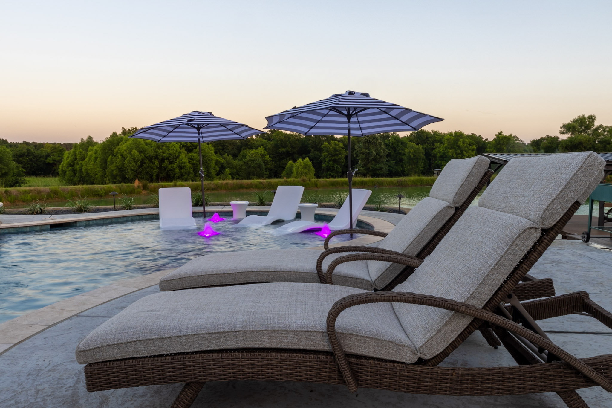 Three white in-pool loungers with striped umbrellas and purple-lit bubblers on a tanning ledge.