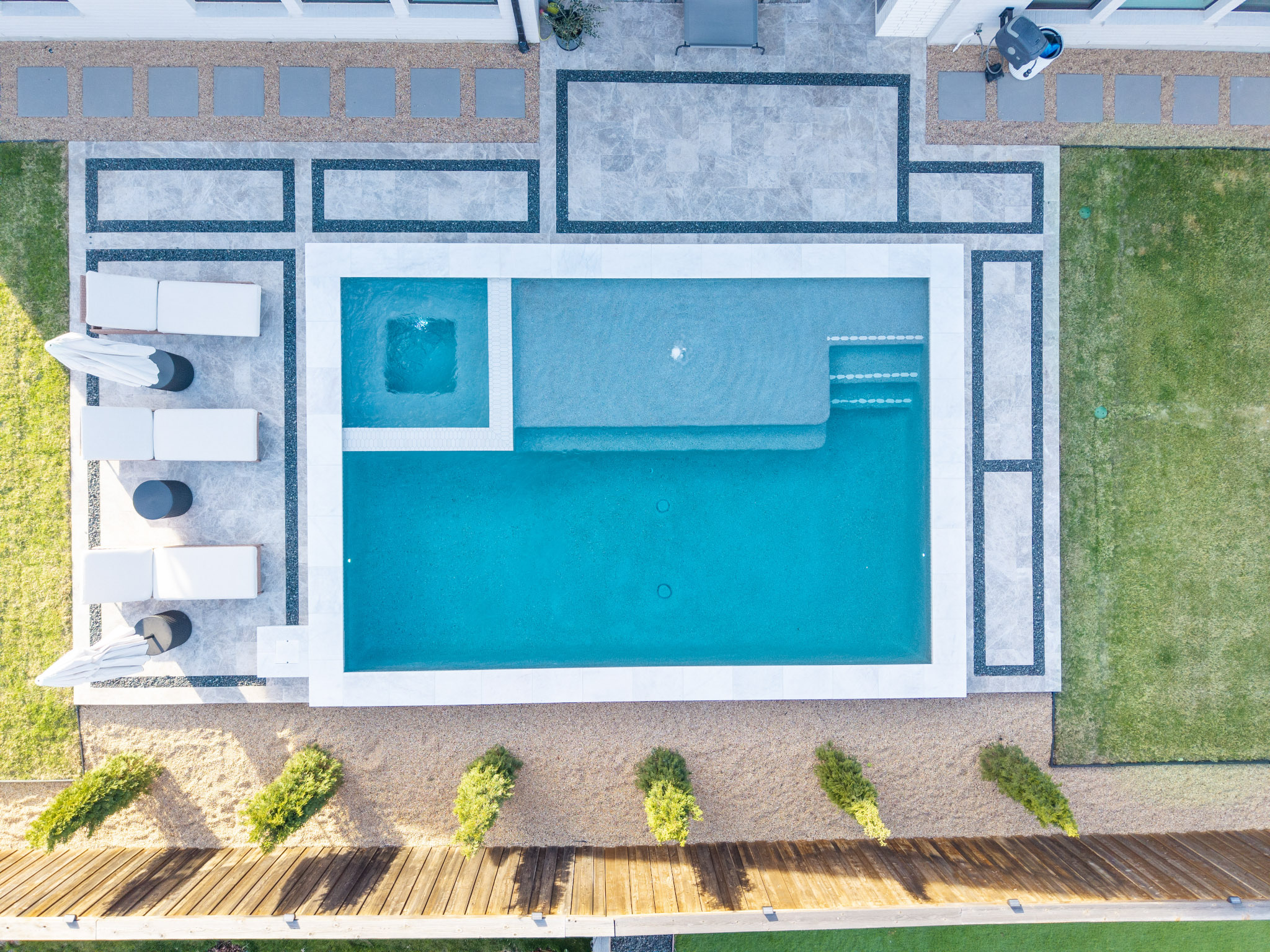 Top-down aerial of rectangular pool with square spa, tanning ledge, steps and geometric patio.