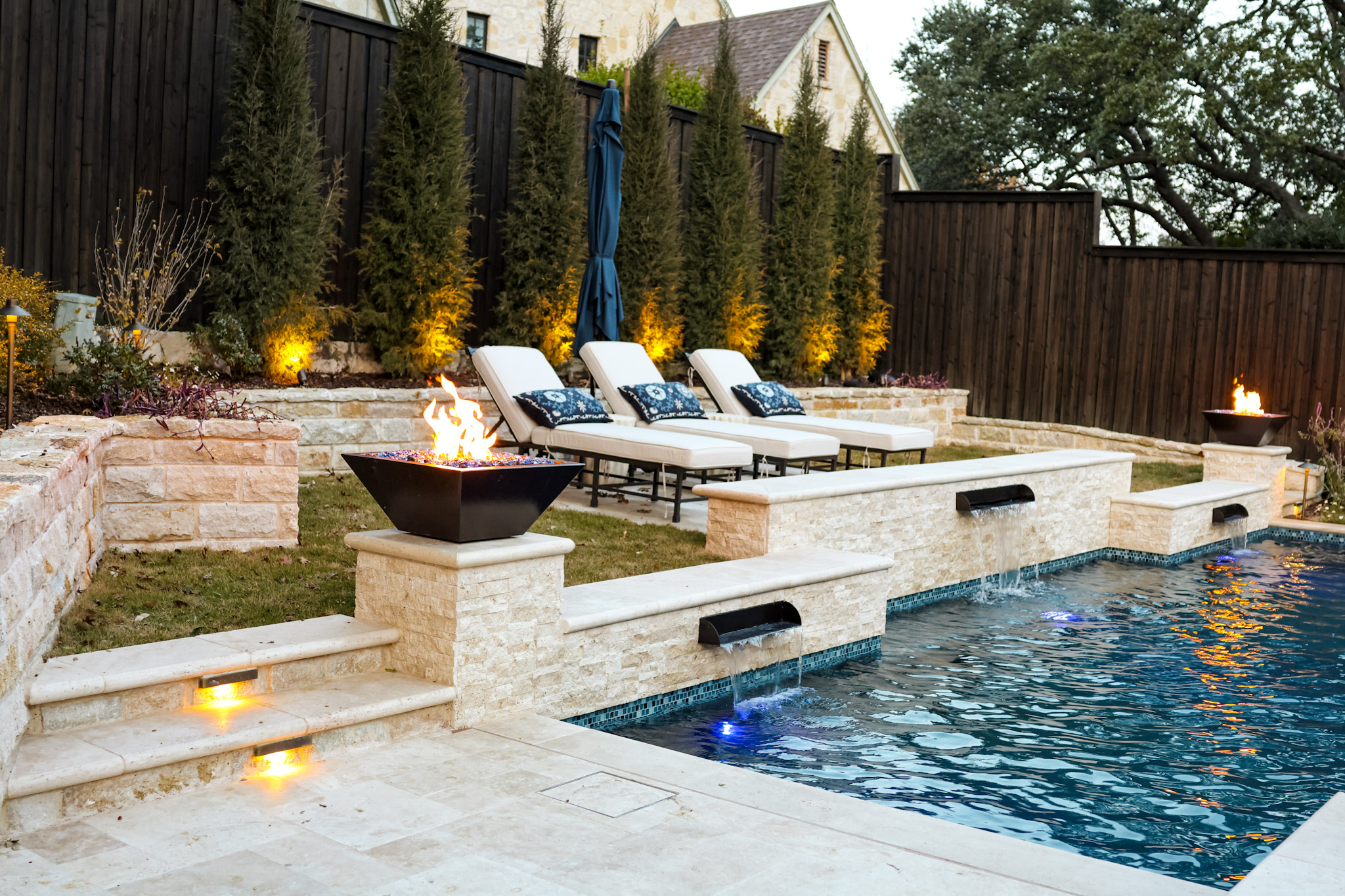 Fire bowl beside stone pool wall with sheer descents and lounge chairs.