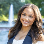 Close-up portrait of a UNT graduate with a fountain in the background