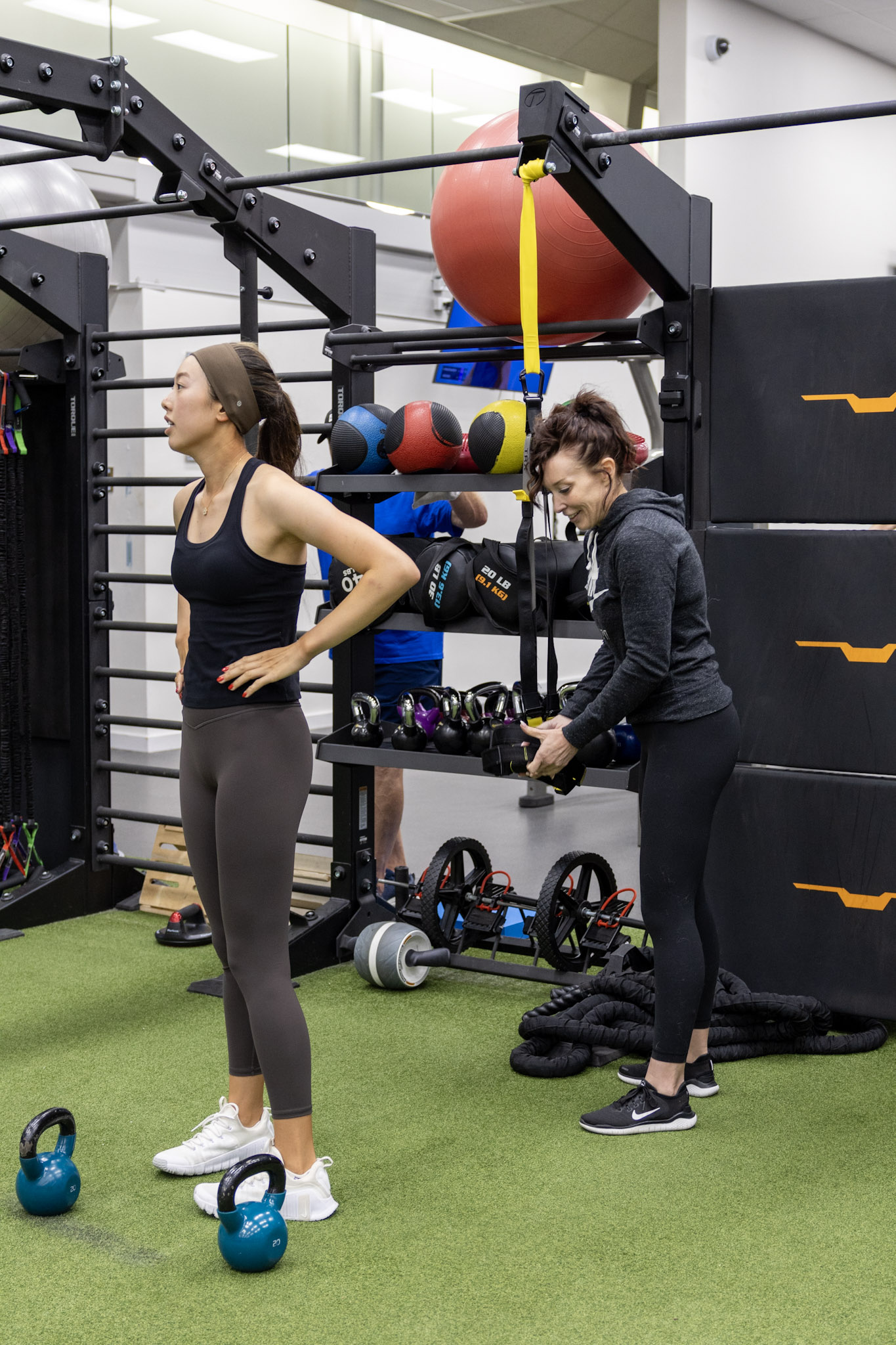 Strength coach instructing an athlete beside kettlebells and resistance equipment.