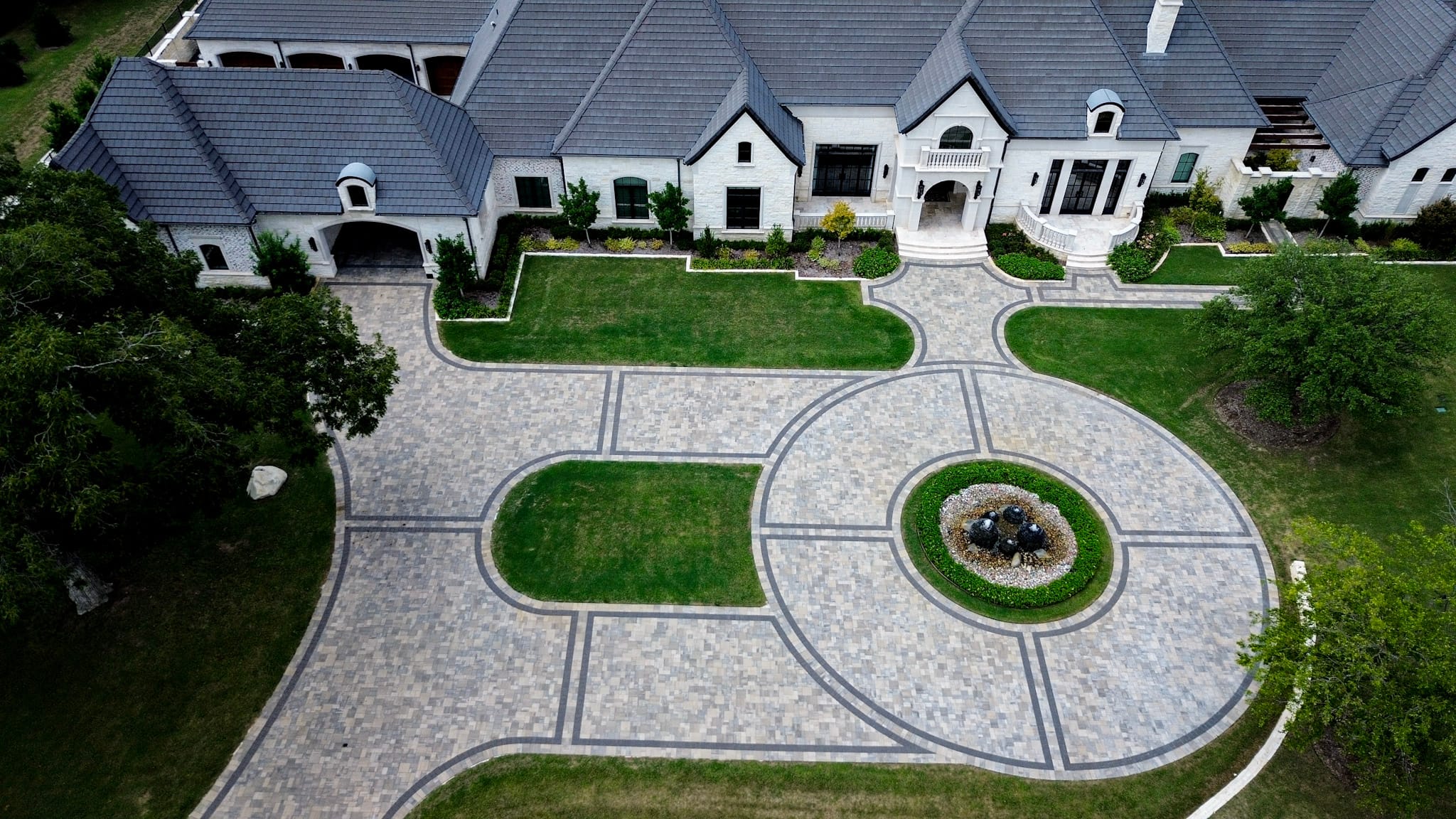 North Texas construction photography from above showing a circular Belgard paver driveway with dark geometric borders.