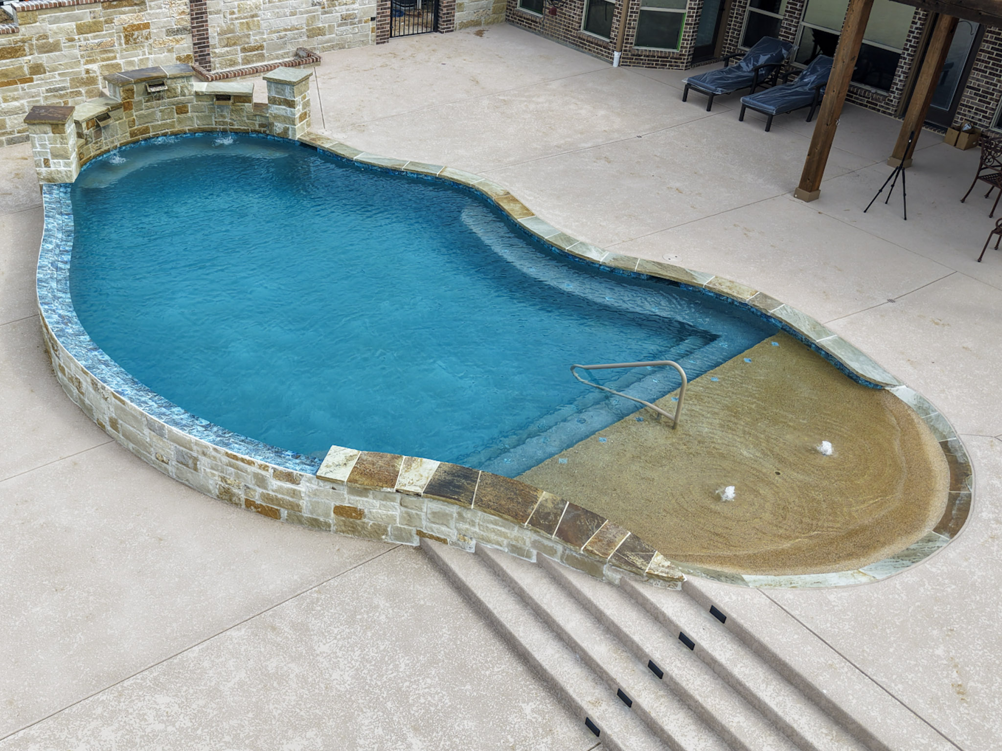 Elevated aerial view of a freeform pool with tanning ledge and stone coping beside a patio.