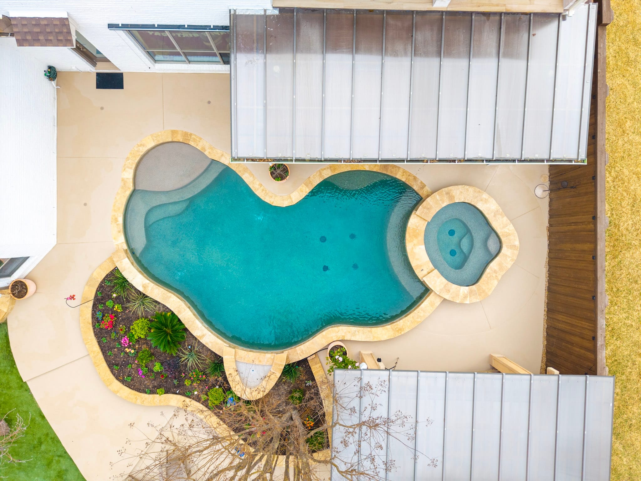 Plano drone photography showing a freeform pool, raised spa, landscaping, patios and covered outdoor living areas.