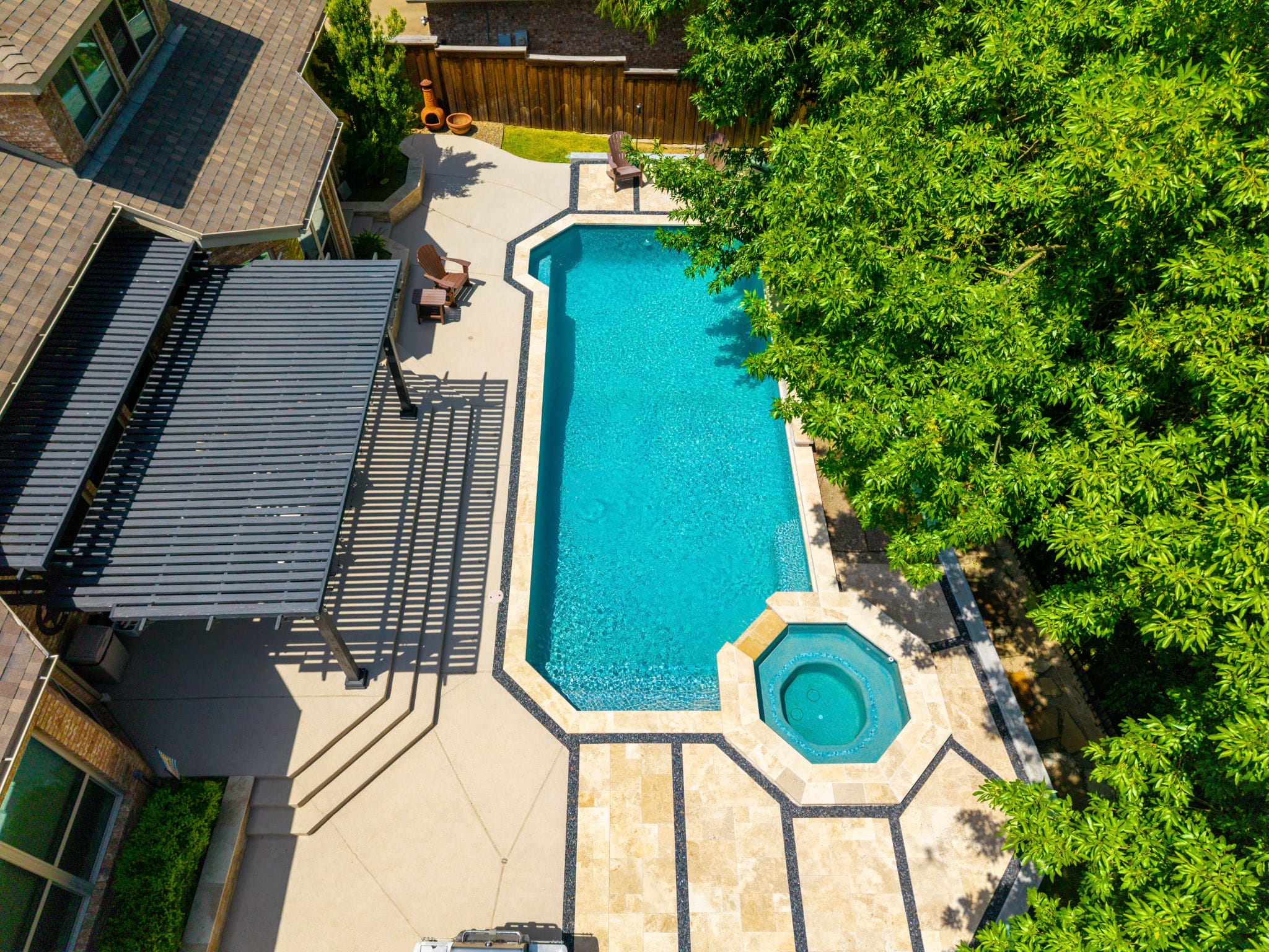 Elevated drone view of a long geometric pool, raised spa and pergola surrounded by mature trees.