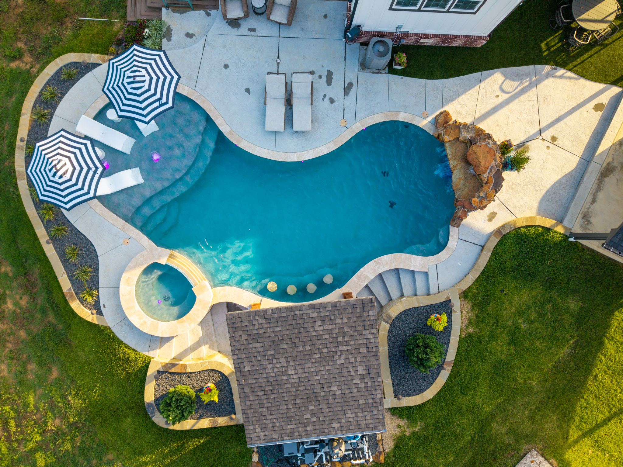 Top-down aerial view of a freeform pool with spa, tanning ledge, waterfall and covered outdoor kitchen.