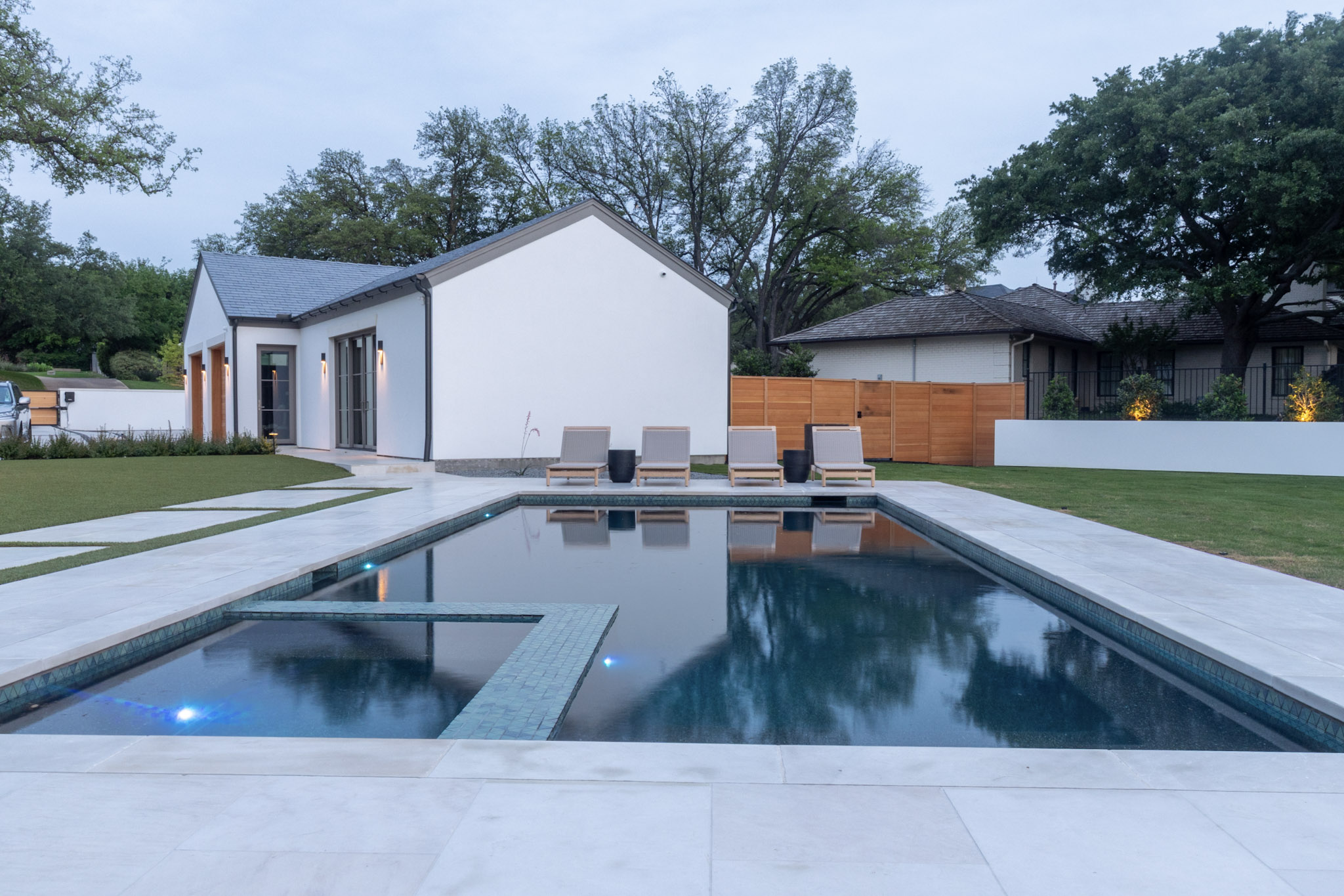 Rectangular luxury pool with integrated spa and blue pool lights at dusk.
