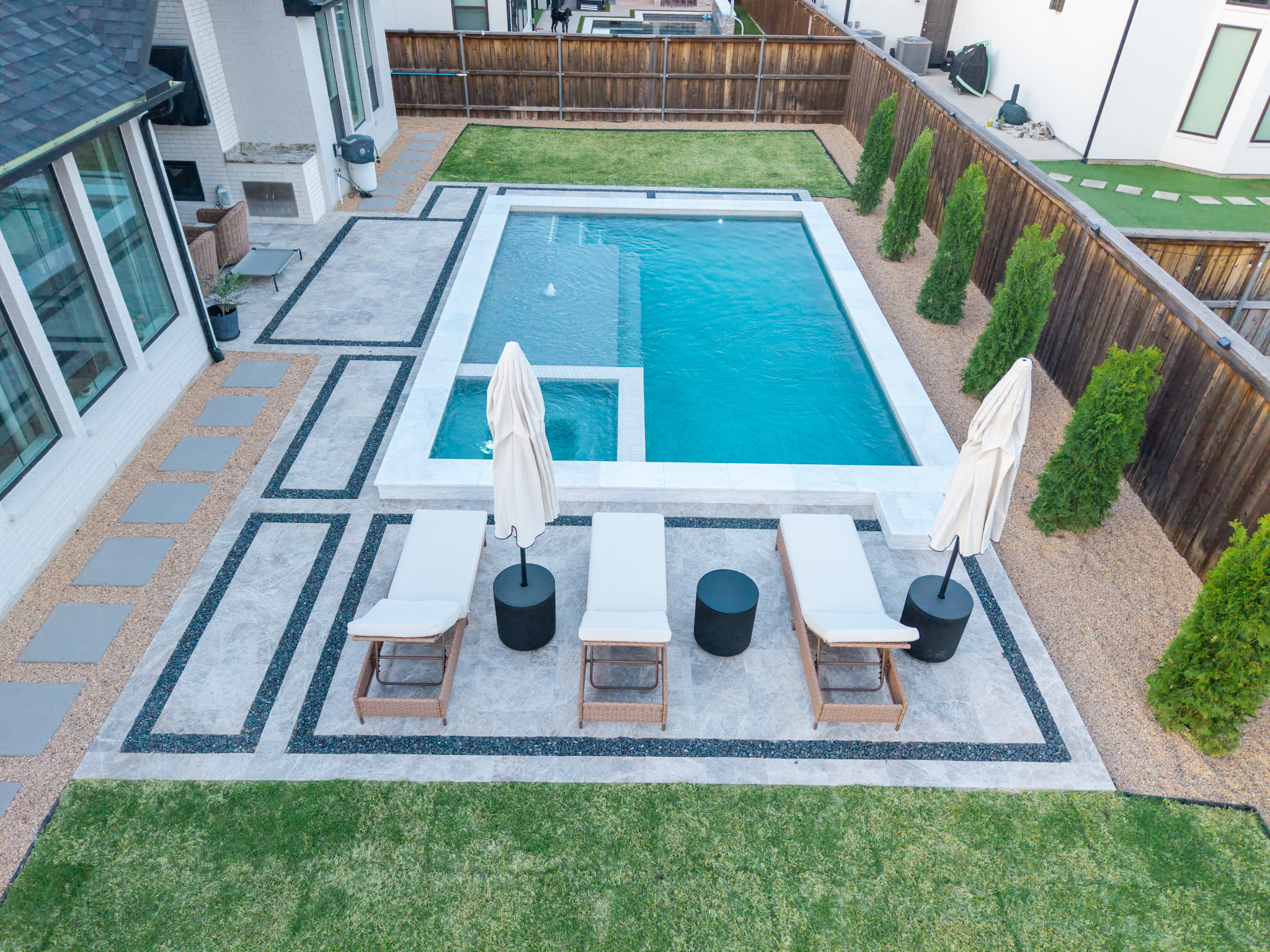 Aerial view of rectangular pool with square spa, tanning ledge, lounge patio and landscaping.