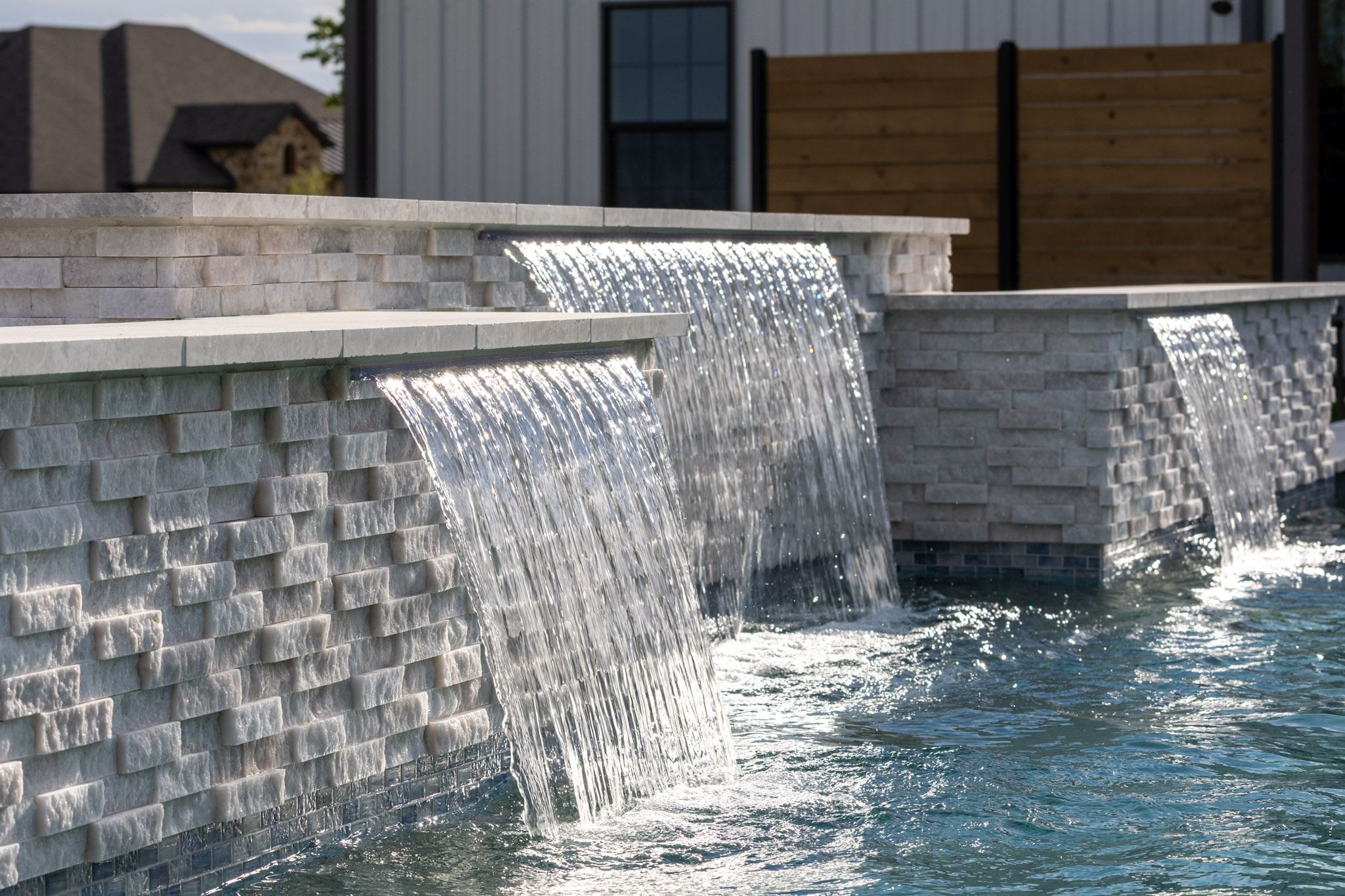 Close view of three sheer descents flowing from a stacked-stone pool wall.