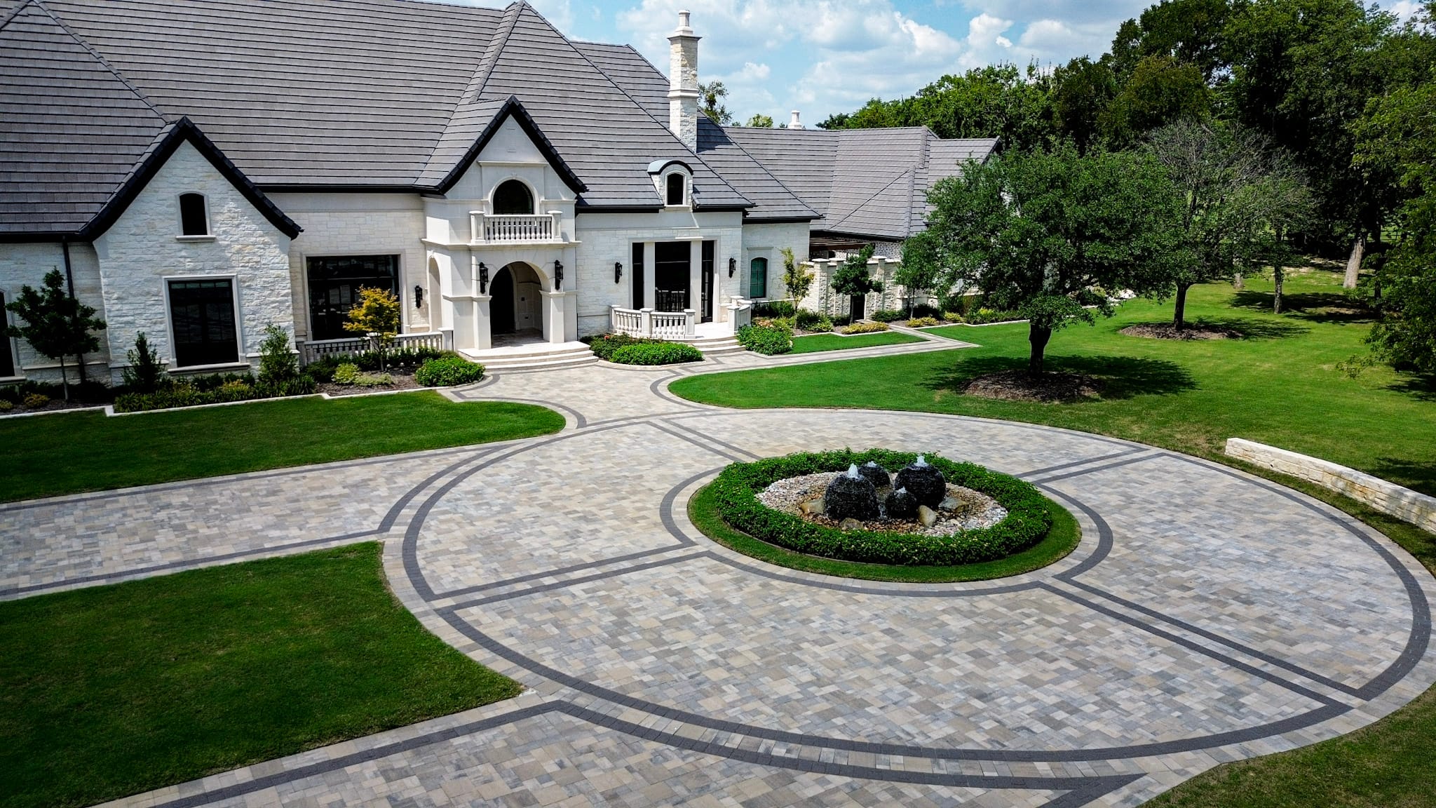 Aerial view of an Allen custom home with circular Belgard paver driveway and landscaped center fountain.