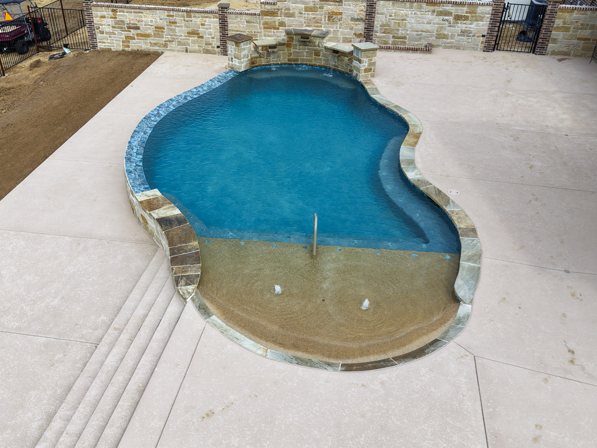 Aerial view of a freeform pool with large tanning ledge, two bubblers and stone water-feature wall.