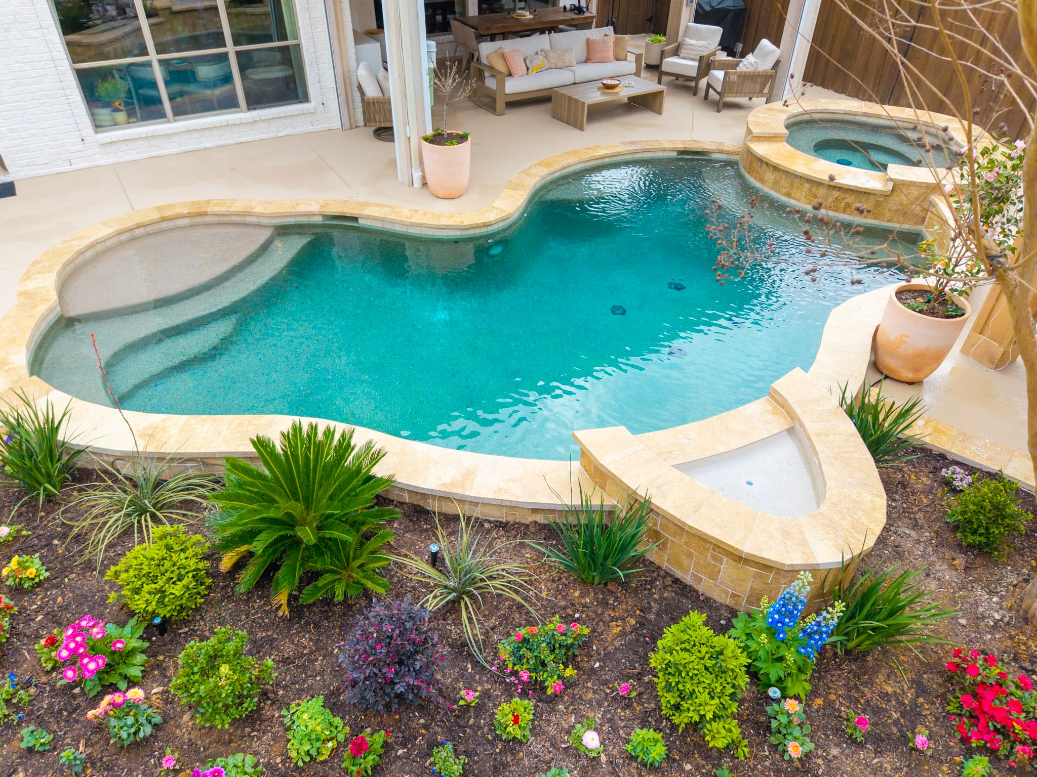 Elevated aerial view of a Plano backyard with freeform pool, raised spa, landscaped beds and covered patio.