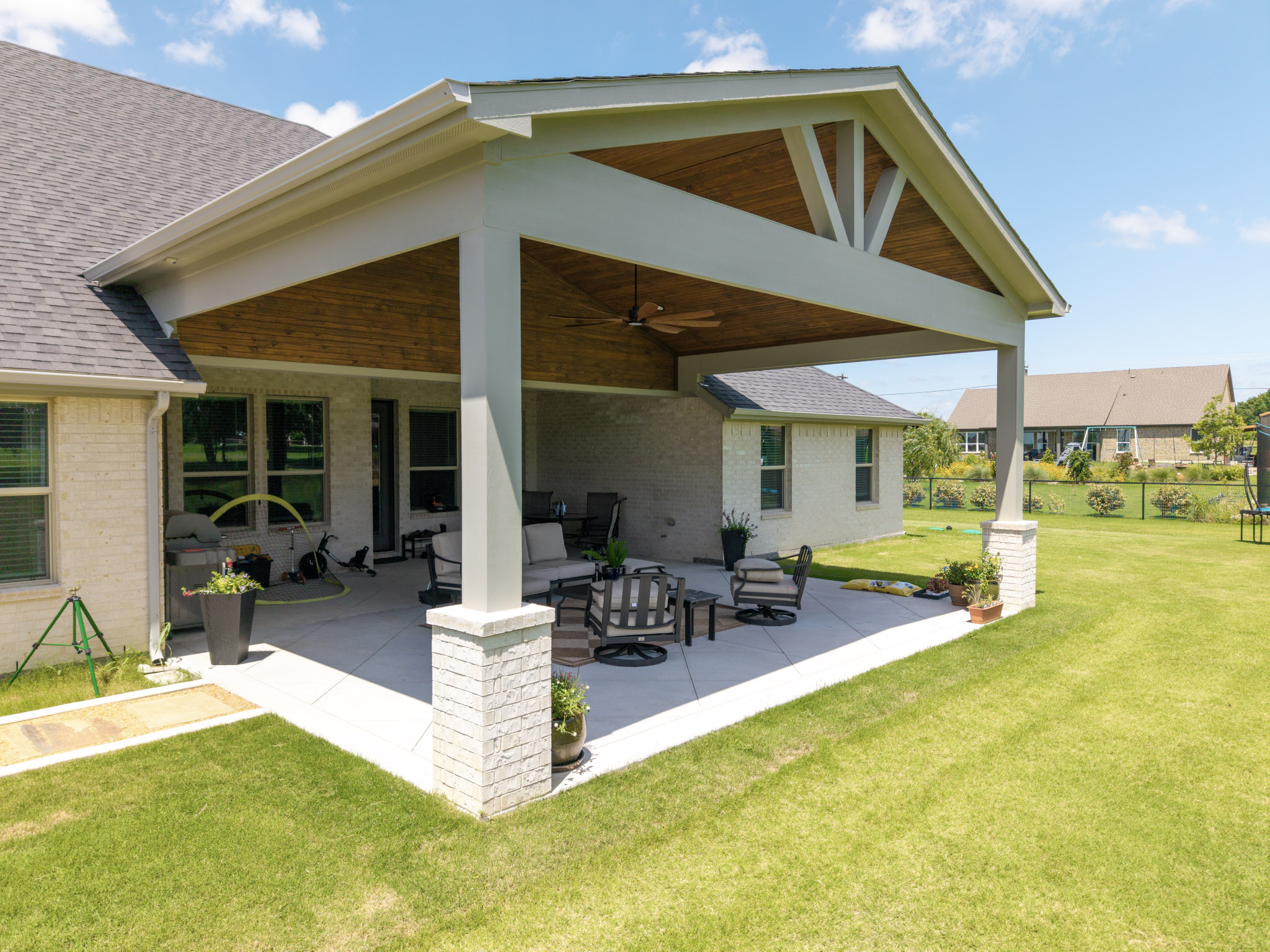 Large gabled covered patio with wood ceiling, decorative framing and masonry-base columns.