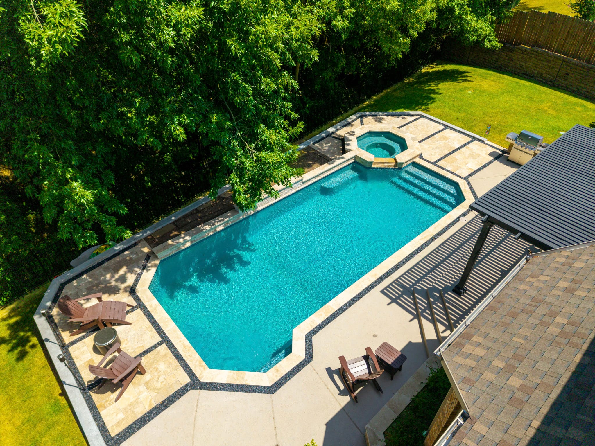 Aerial view of McKinney pool, raised spa, pergola, light decking and wooded backyard.