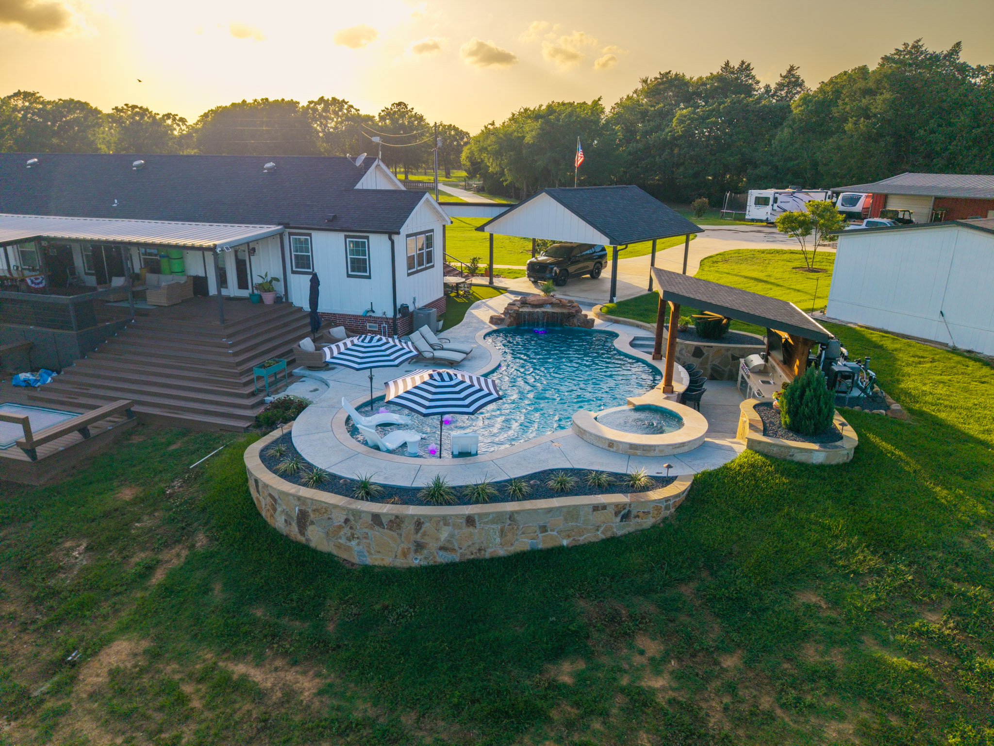 Sunset aerial view of a freeform pool with spa, waterfall, tanning ledge and covered outdoor kitchen.