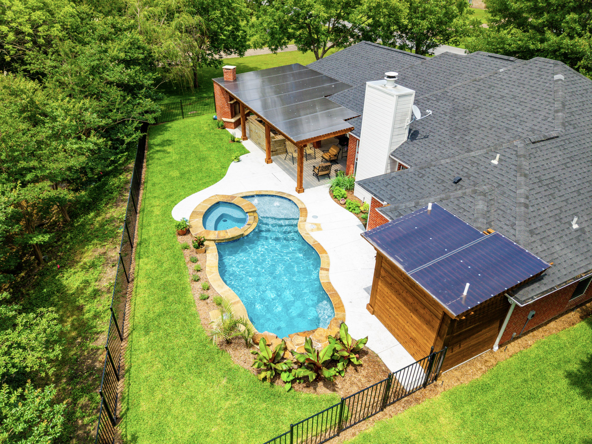 Aerial view of a freeform pool, raised spa, outdoor living areas and landscaped backyard.
