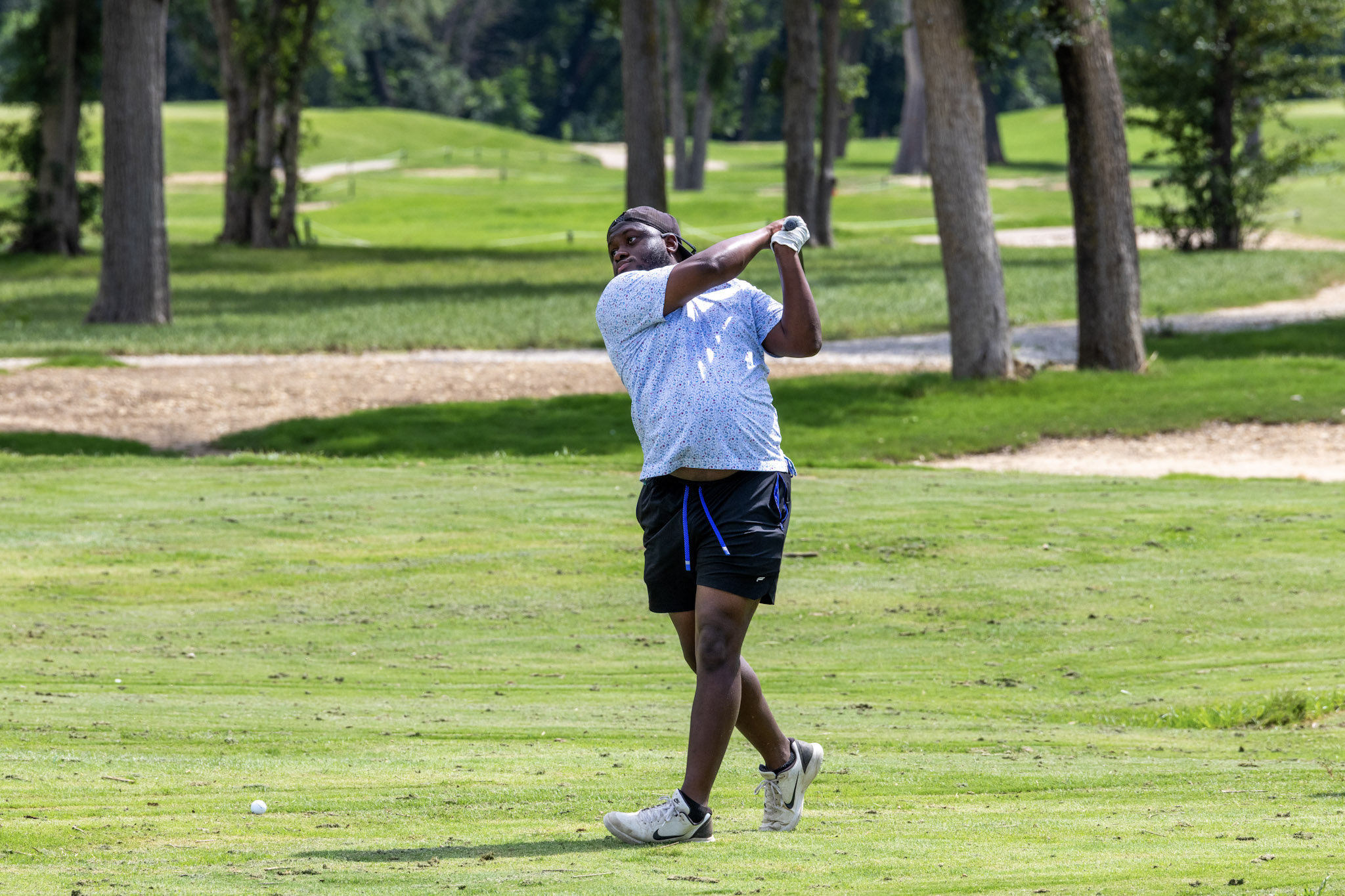 Golfer finishing his swing on a tree-lined golf course