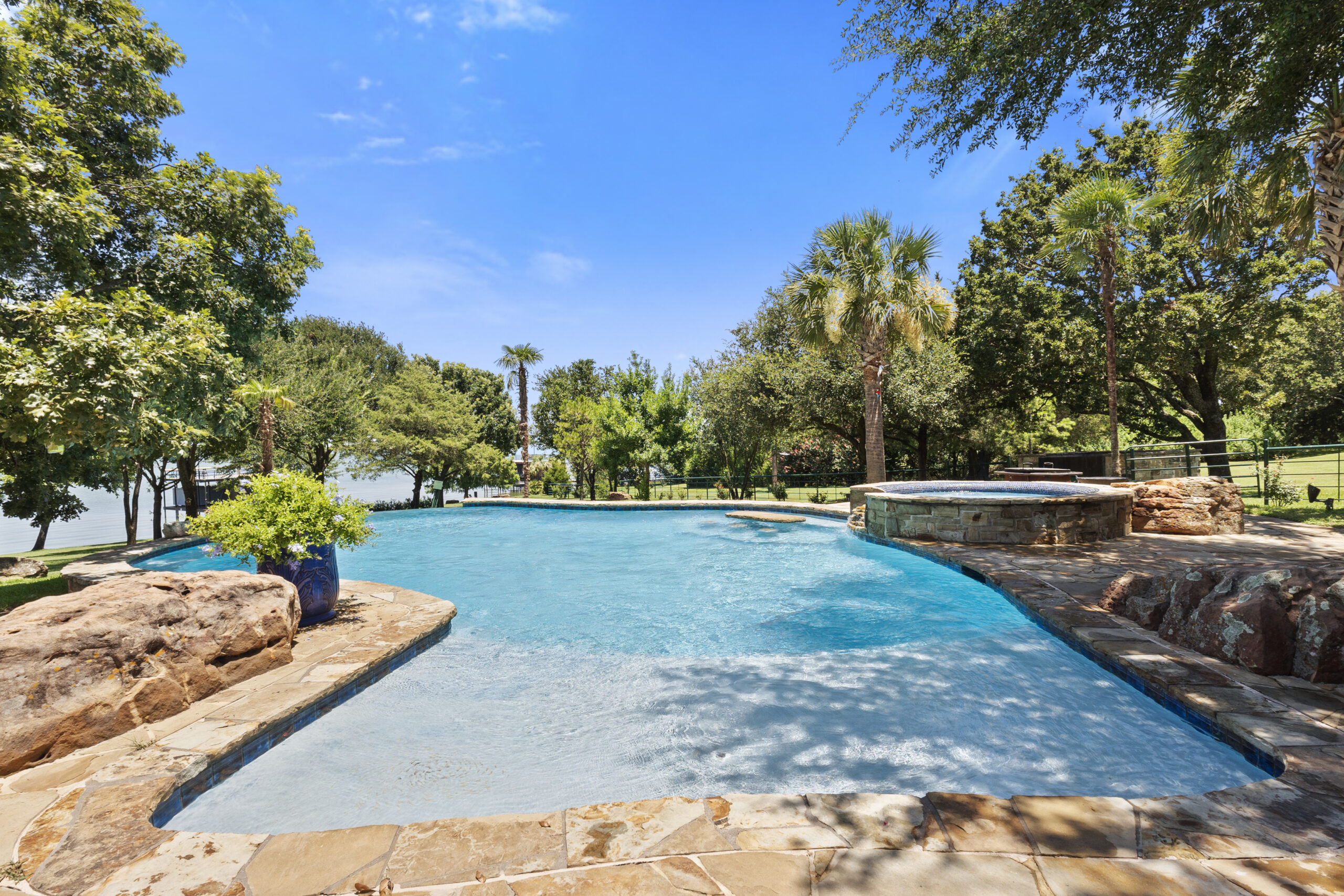 Shallow area of a freeform pool with natural stone edges, trees and lake beyond.