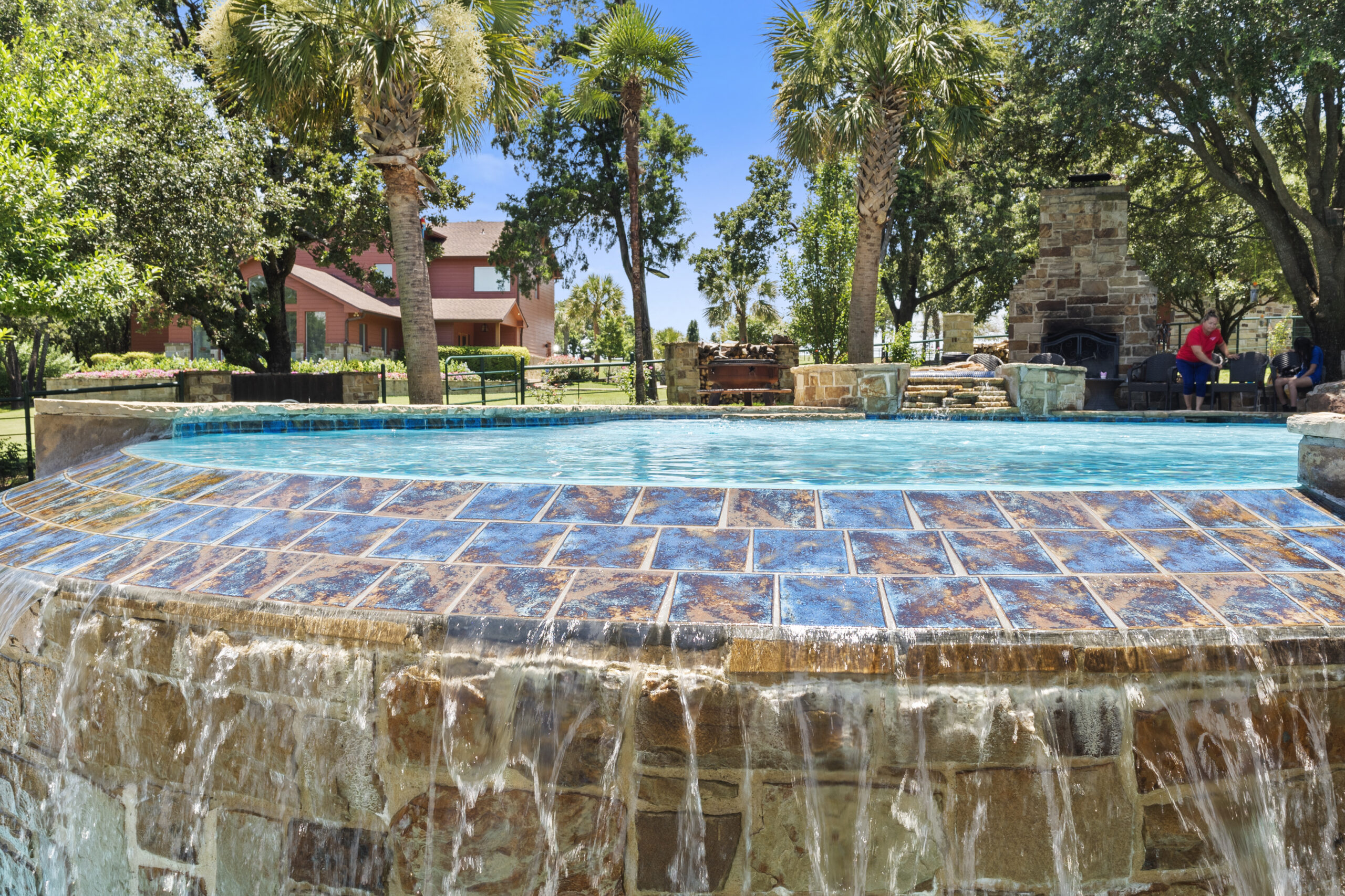Wide tiled pool overflow with water cascading down a natural-stone wall.