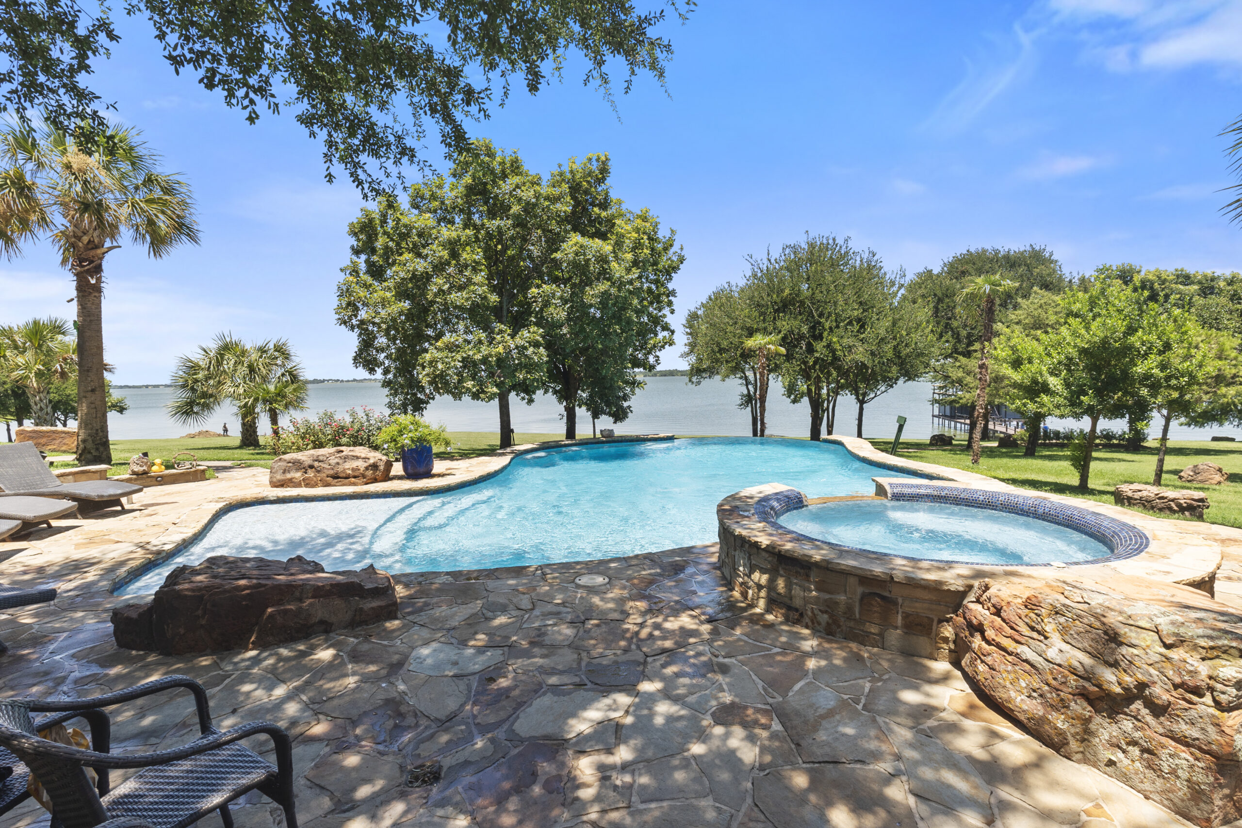 Wide lakefront backyard with freeform pool, raised circular spa and natural-stone patio.