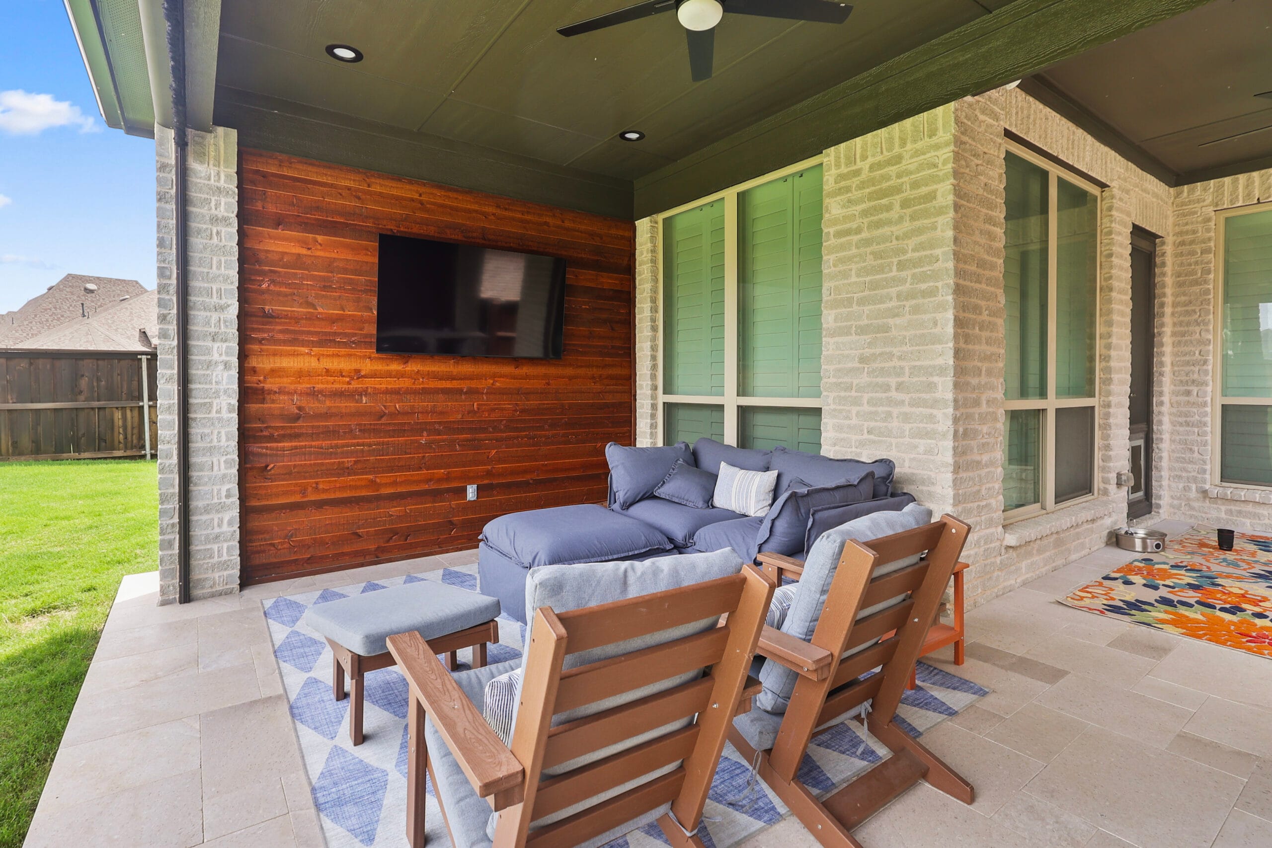 Custom covered patio with seating, TV wall, ceiling fan, and travertine flooring
