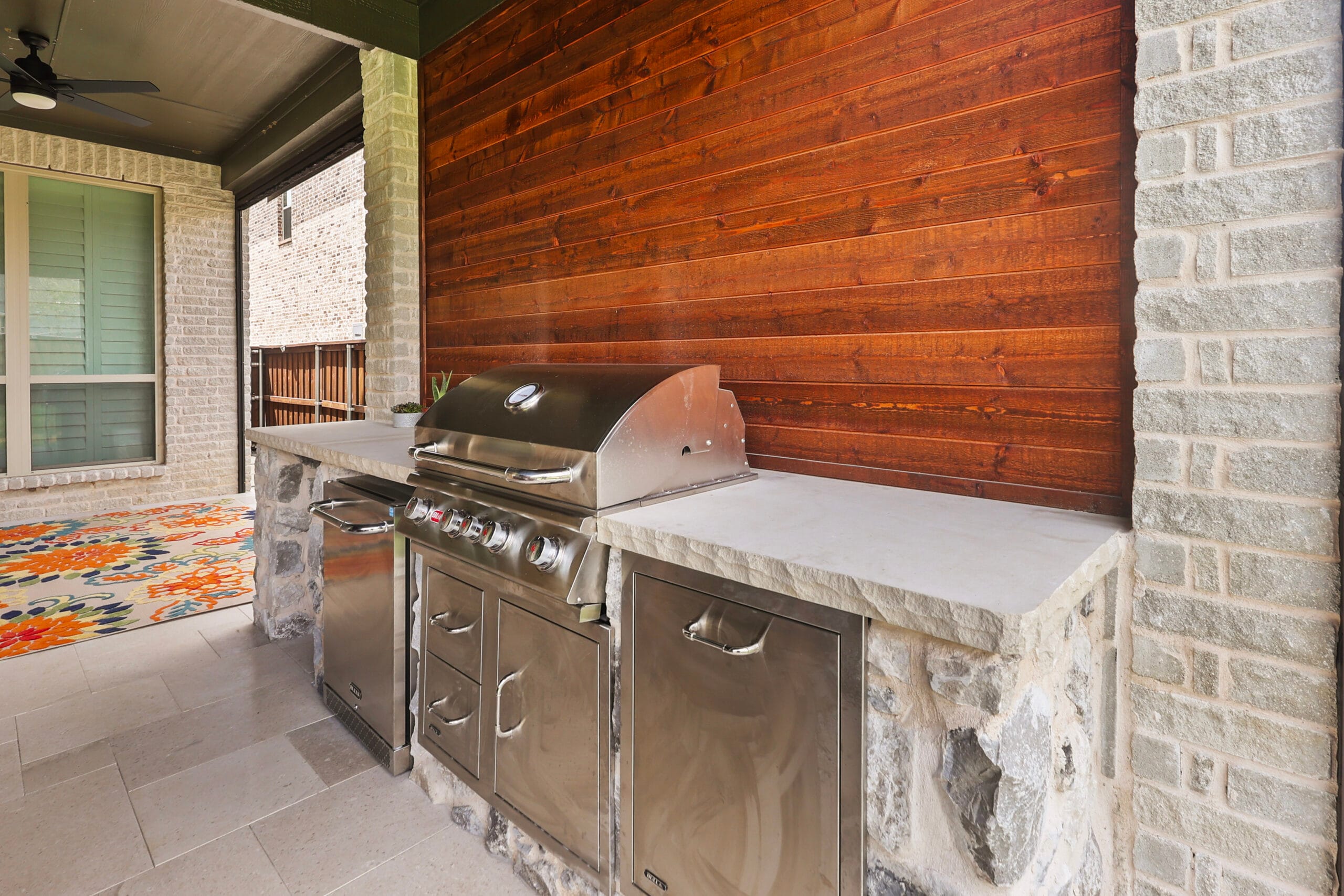 Stainless steel outdoor kitchen built into stone cabinetry under a patio cover