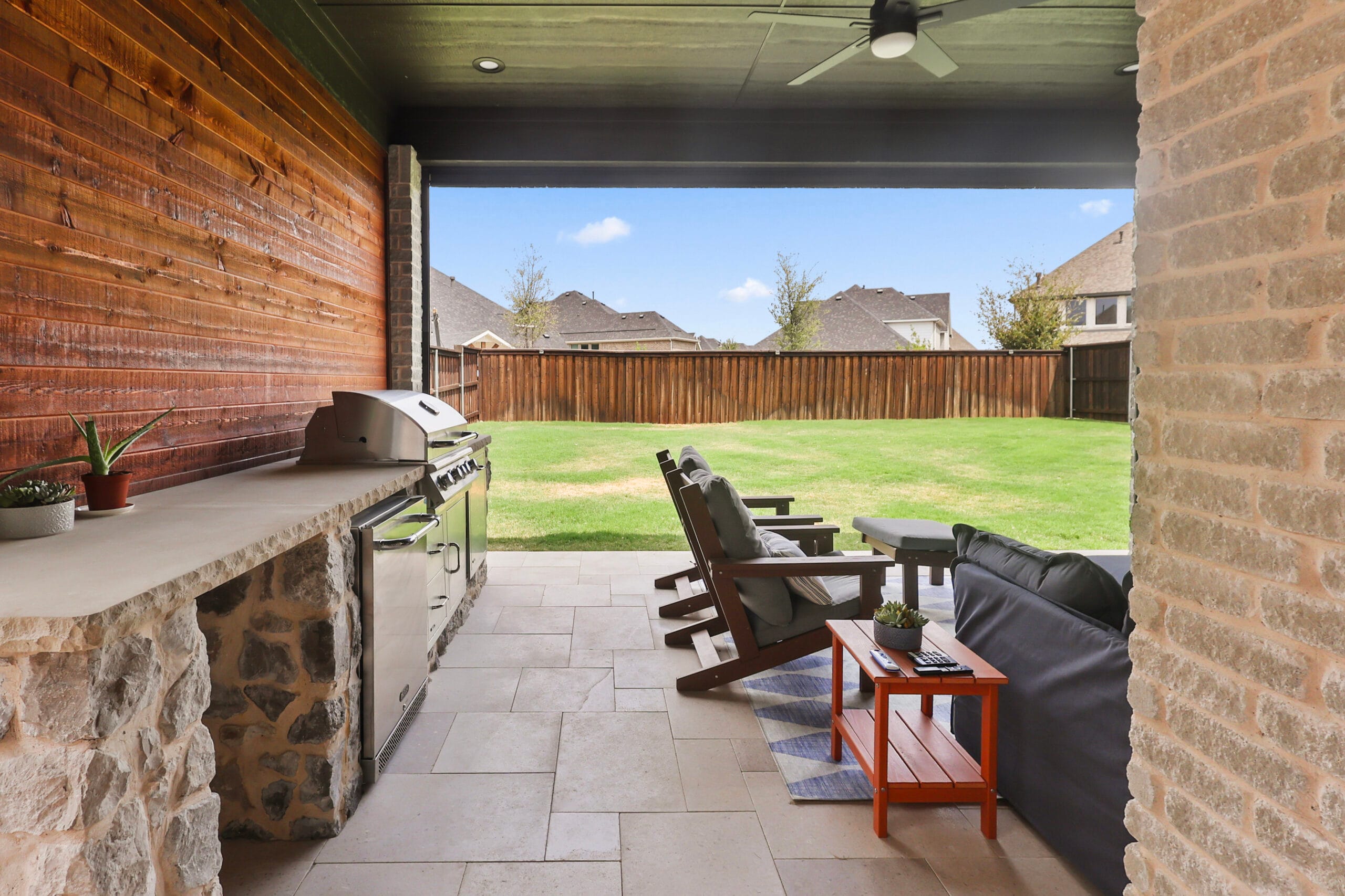 Wide view of a covered patio with outdoor kitchen, seating, and backyard in The Colony
