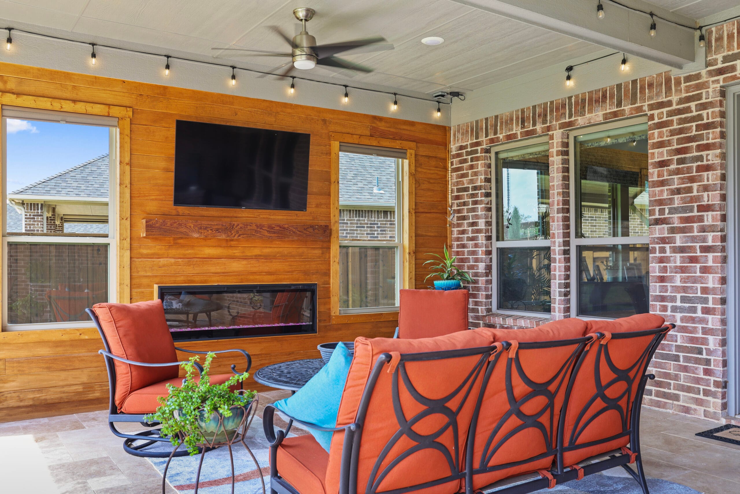 Furnished covered patio with TV wall, fireplace, ceiling fan, and string lights